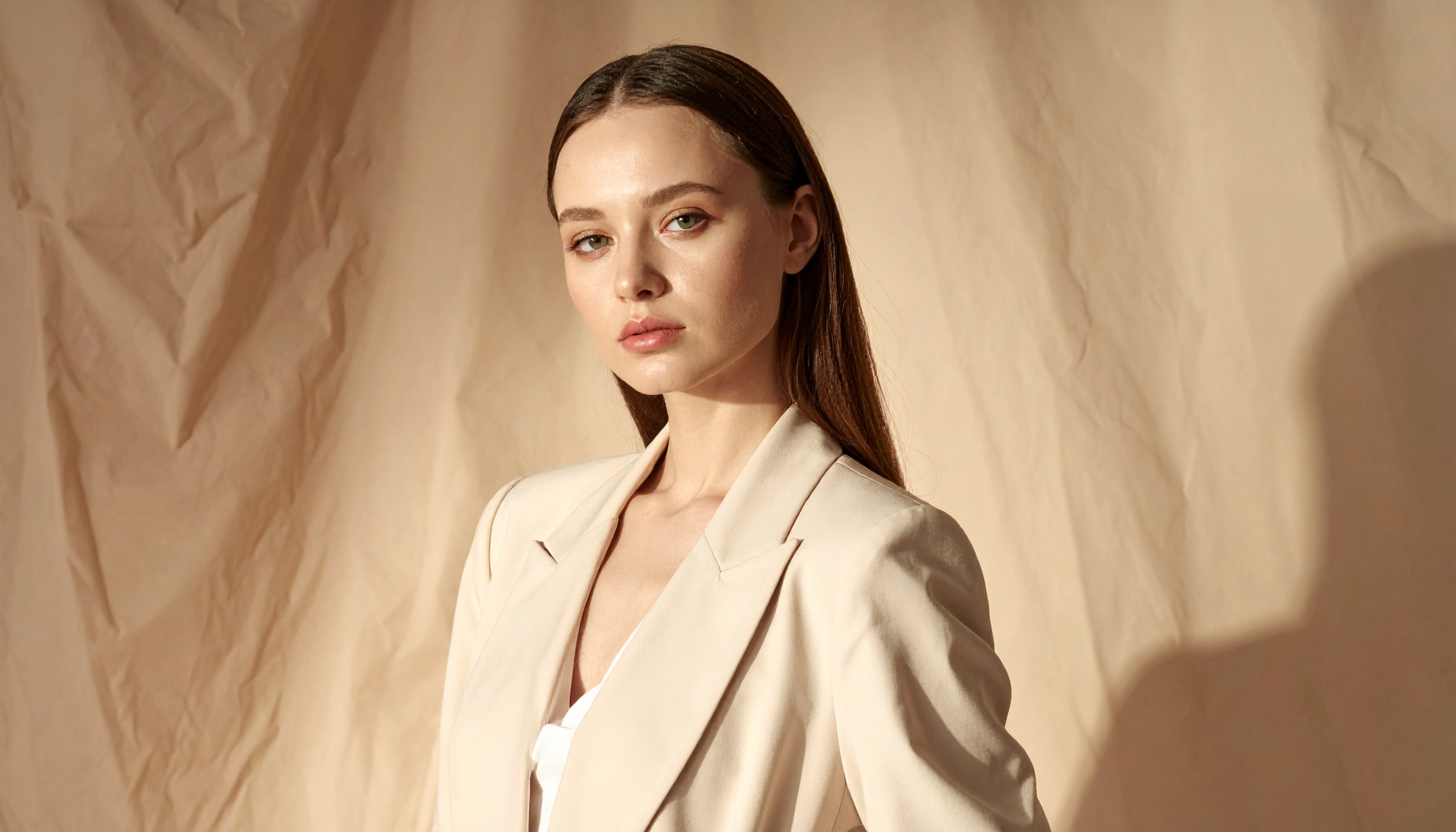 A woman confidently wears a cream-colored blazer against a textured beige backdrop
