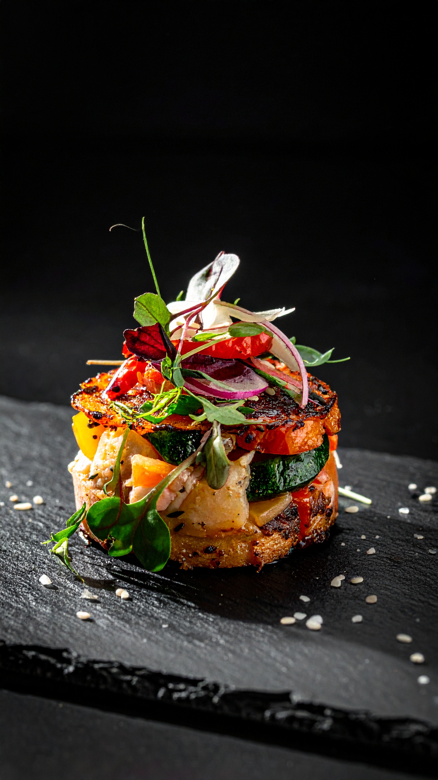 A gourmet vegetable stack sits elegantly on a dark slate plate
