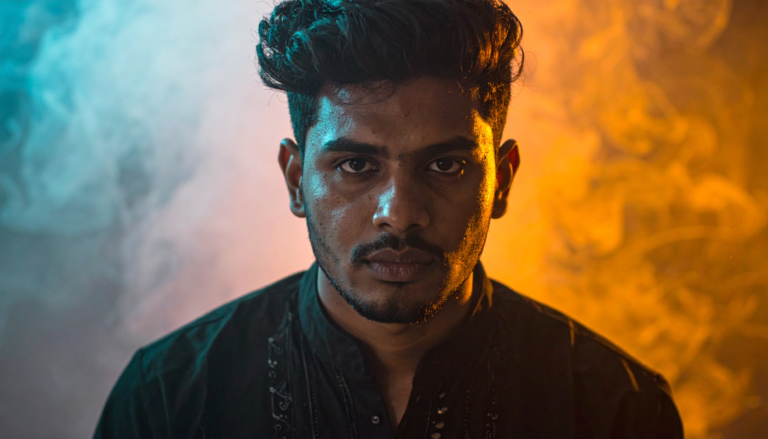 A man stands against a dramatic backdrop of contrasting blue and orange smoke