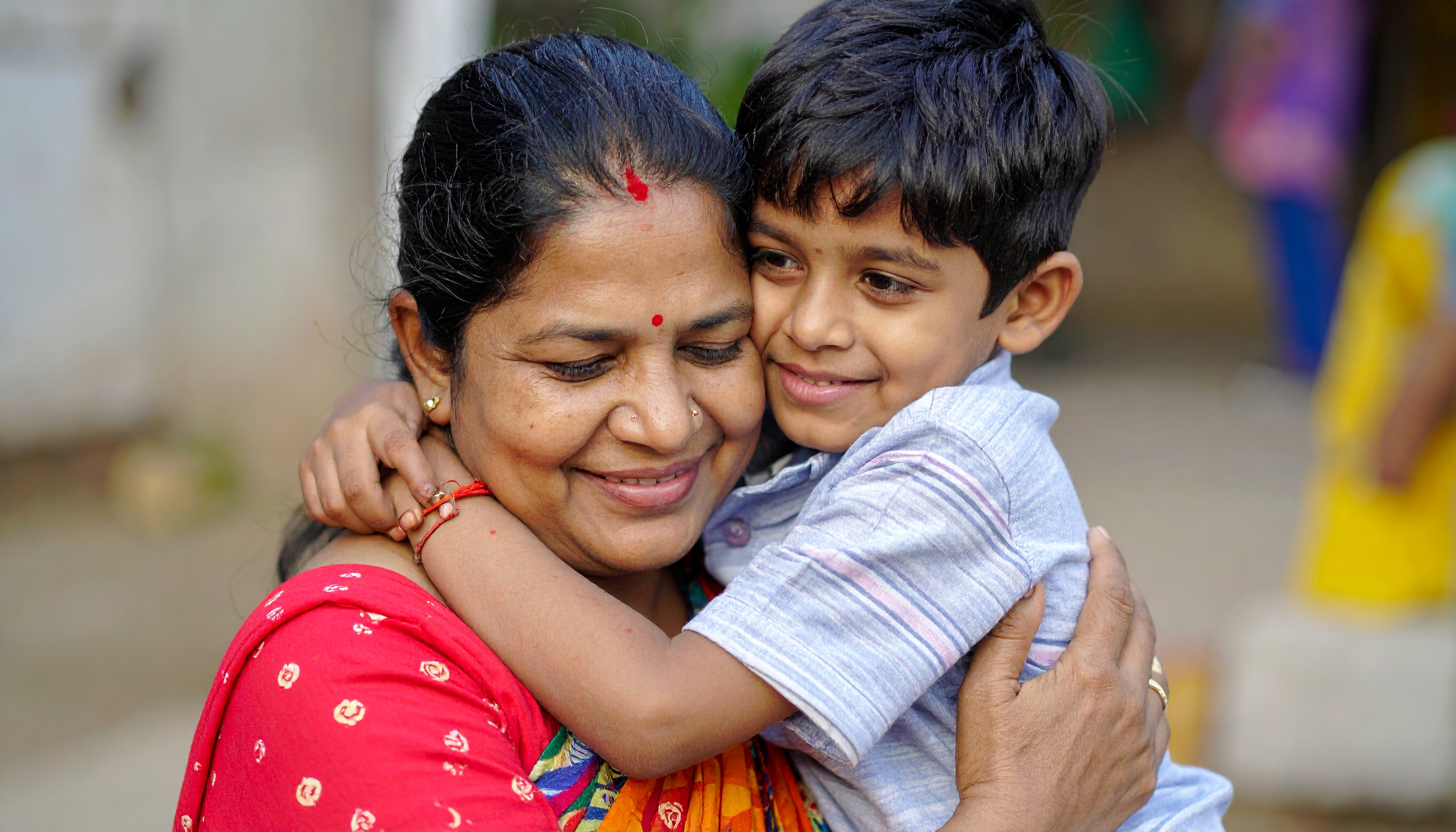 Uma mulher abraça carinhosamente uma criança, expressando um vínculo de amor e segurança. Esta imagem é ideal para campanhas que promovem valores familiares ou produtos voltados para o bem-estar familiar. Destaca-se pela expressão de felicidade e proximidade entre os dois, com cores vibrantes no vestuário da mulher. Pode ser usada em contextos de marketing que enfatizam a importância das relações familiares. A imagem transmite uma sensação de calor e autenticidade, ideal para fortalecer mensagens emocionais.