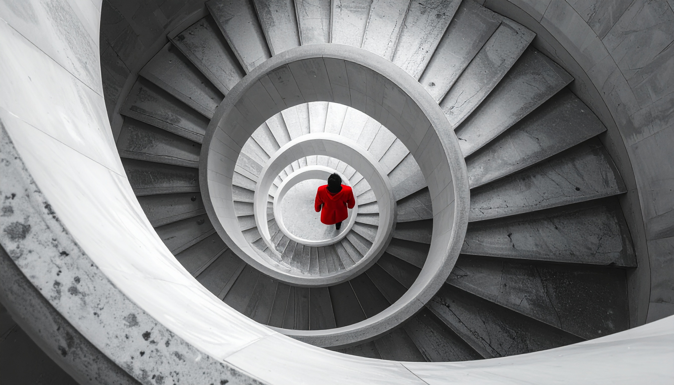 A person in a red coat descends a spiral staircase, creating a striking contrast against