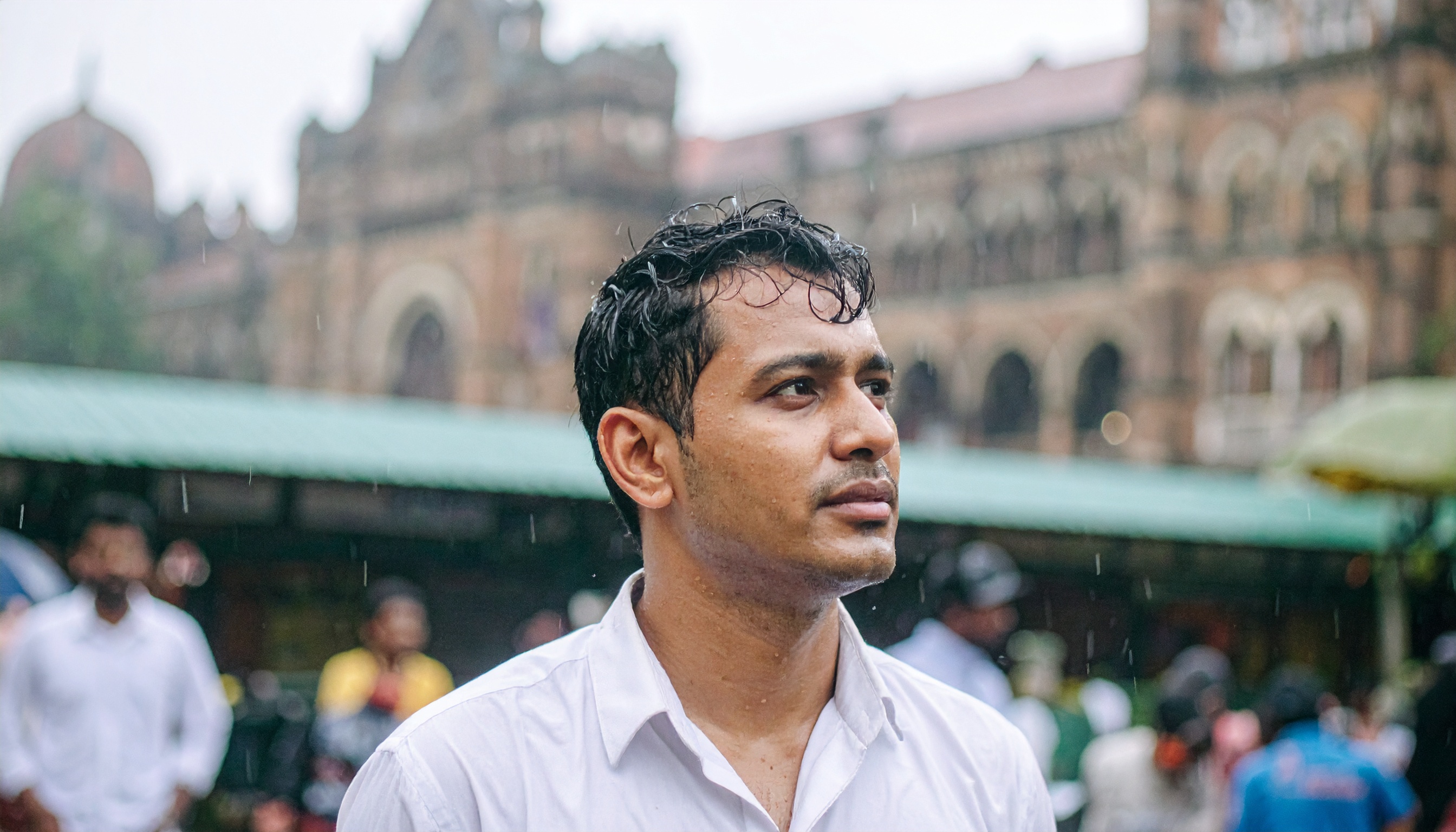 A man stands in the rain, with a historic building in the background
