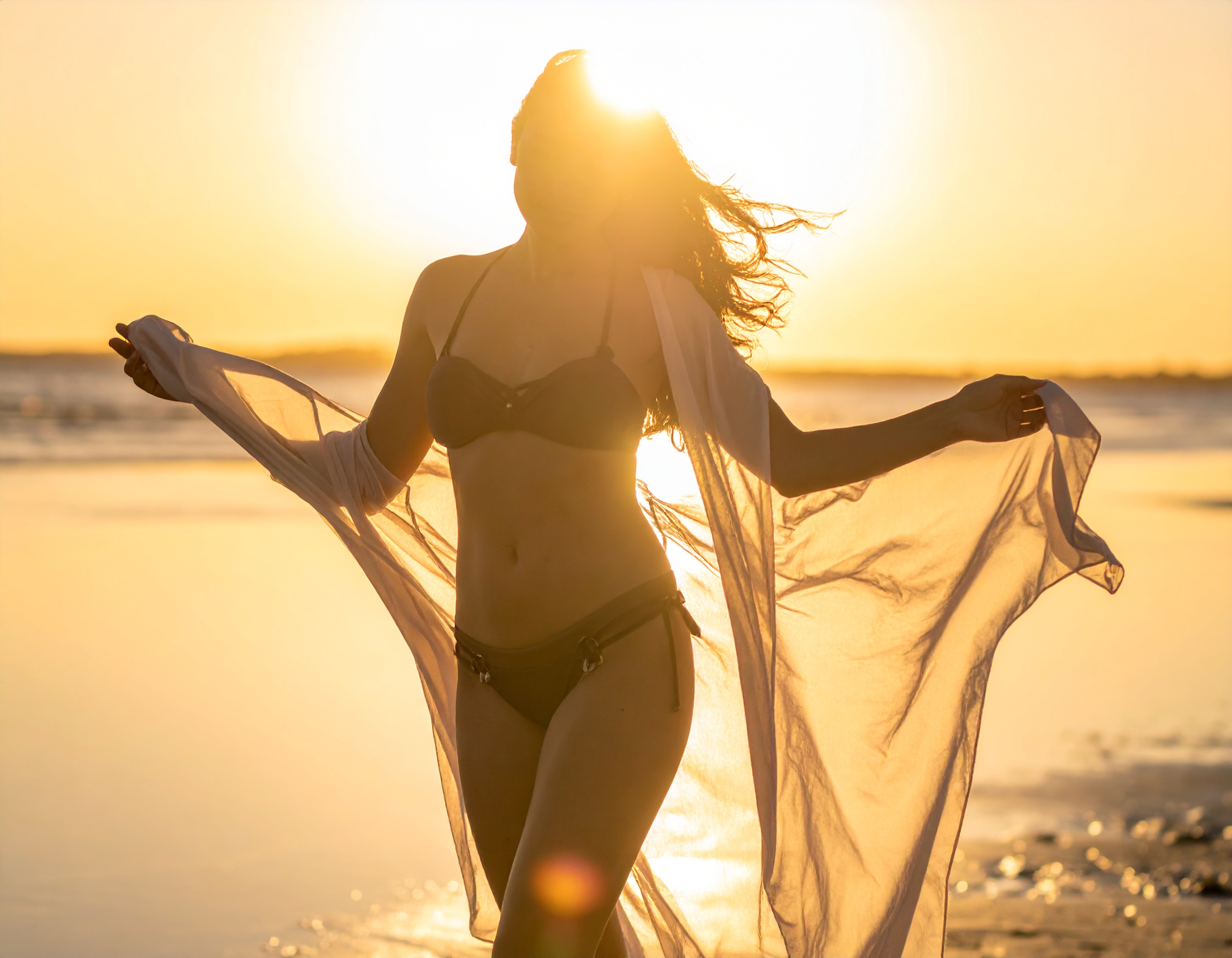 A silhouette of a woman in a bikini with a sheer cover-up is set against