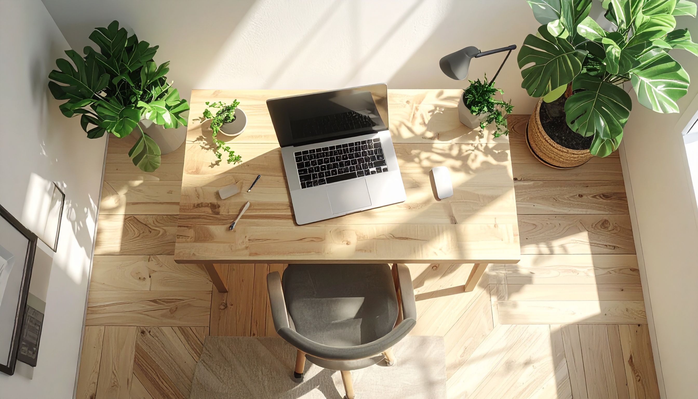 Uma mesa de escritório iluminada por luz natural, com laptop aberto e acessórios organizados, cercada por plantas verdes vibrantes, criando um ambiente de trabalho sereno e minimalista. O piso de madeira clara complementa a composição, enquanto a iluminação suave projeta sombras agradáveis, conferindo uma atmosfera organizada e tranquila.