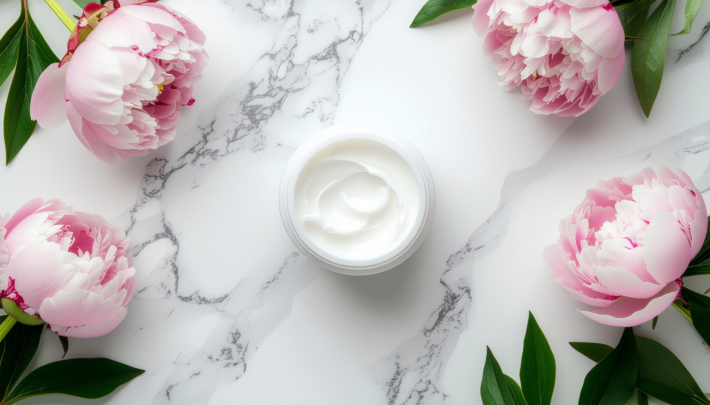 Creme em pote branco centralizado sobre superfície de mármore, cercado por peônias rosas e folhas verdes. Composição simétrica e delicada, com iluminação suave e tons claros.