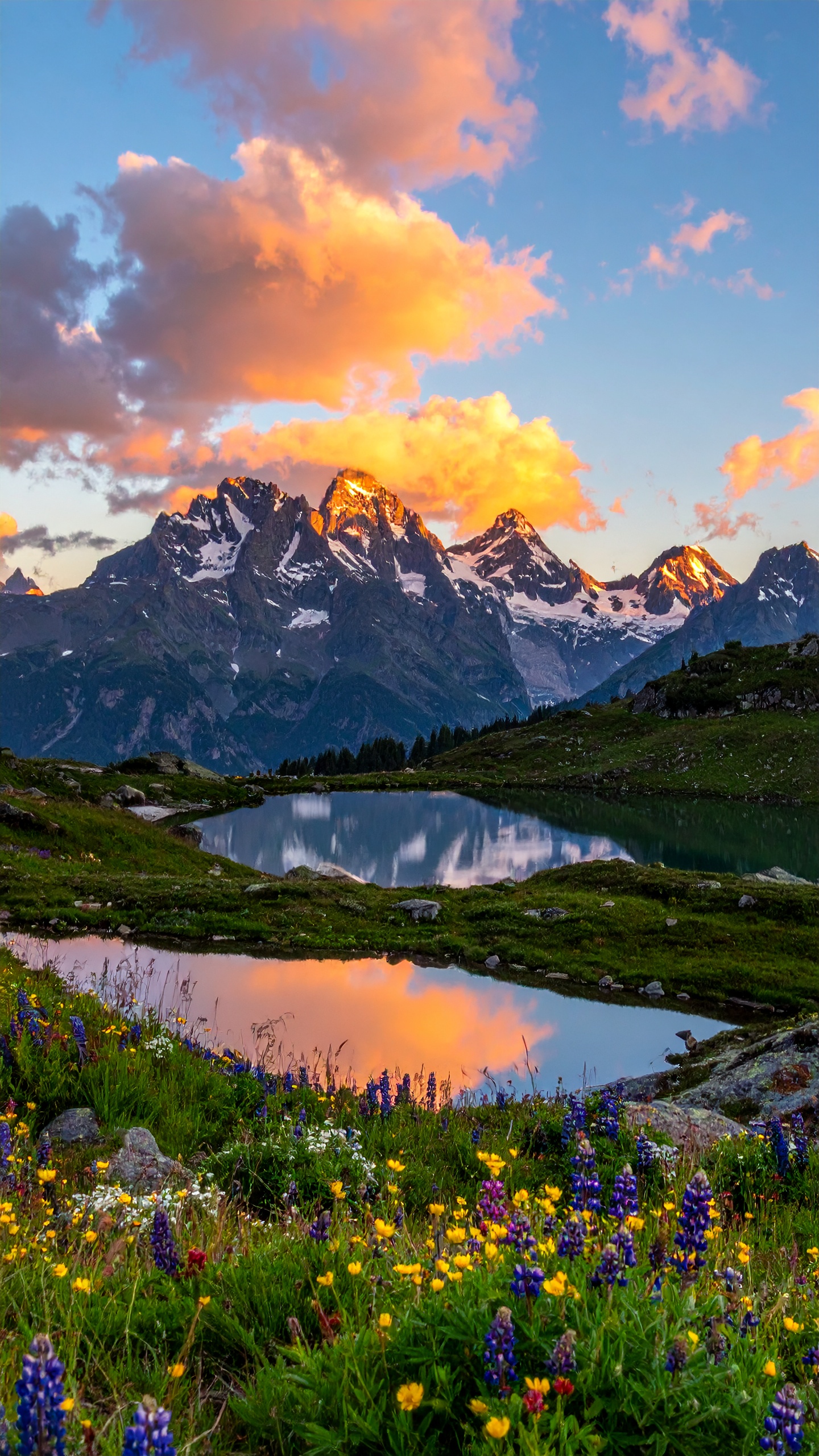 A serene alpine landscape features a tranquil lake reflecting towering snow-capped mountains under a