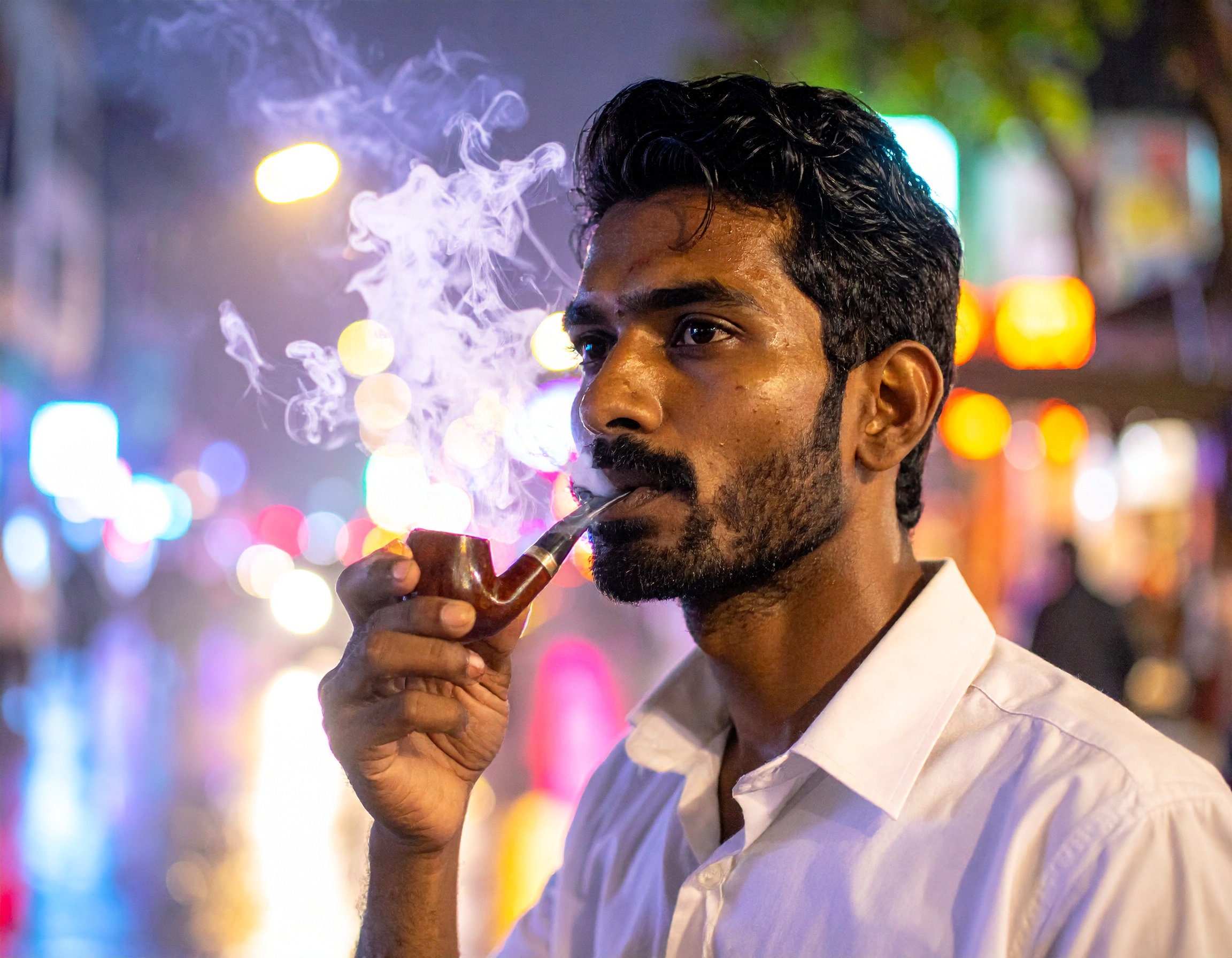 A man enjoys smoking a pipe on a vibrant city street at night