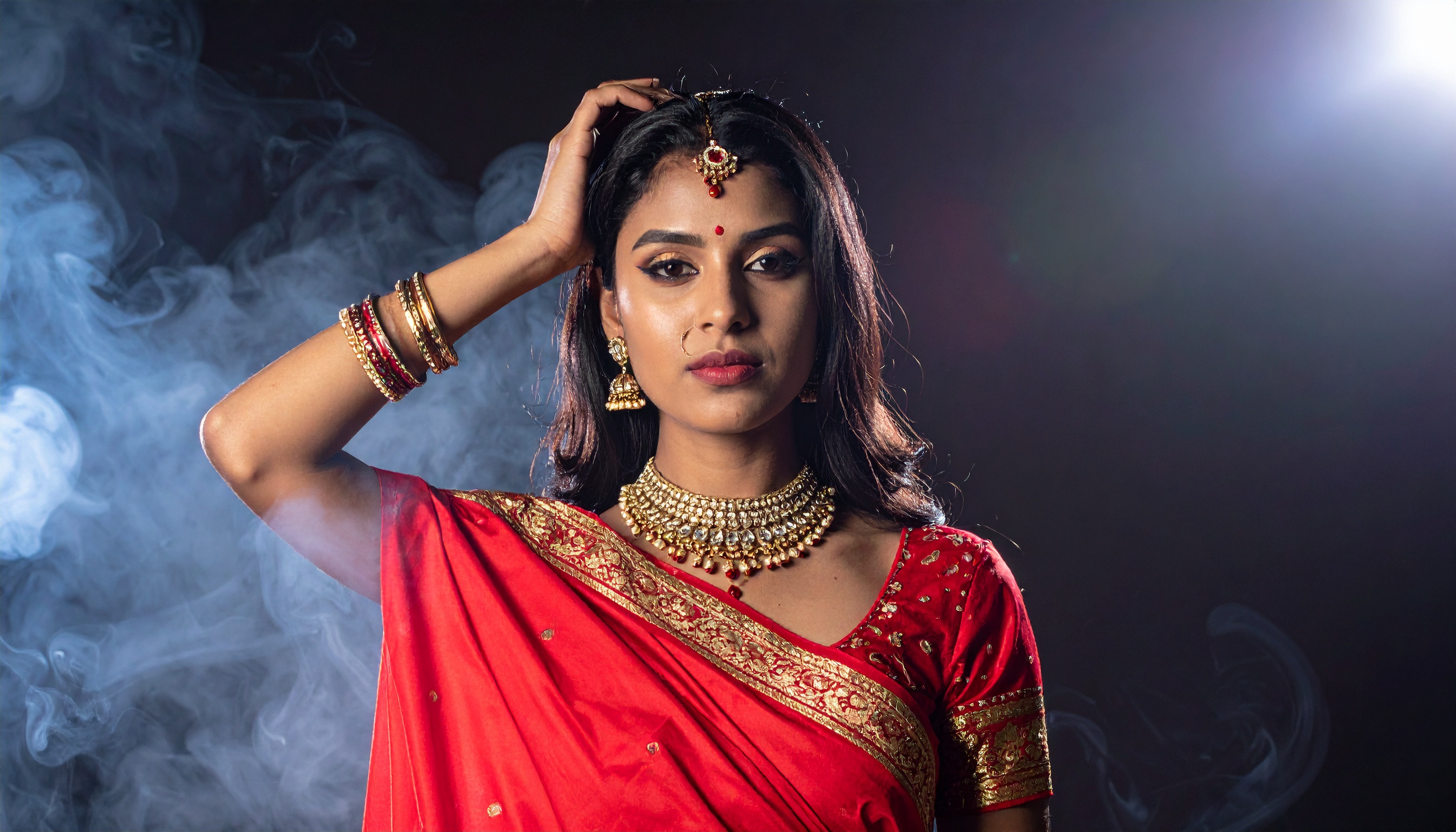 A woman adorned in a stunning red saree is complemented by intricate gold jewelry