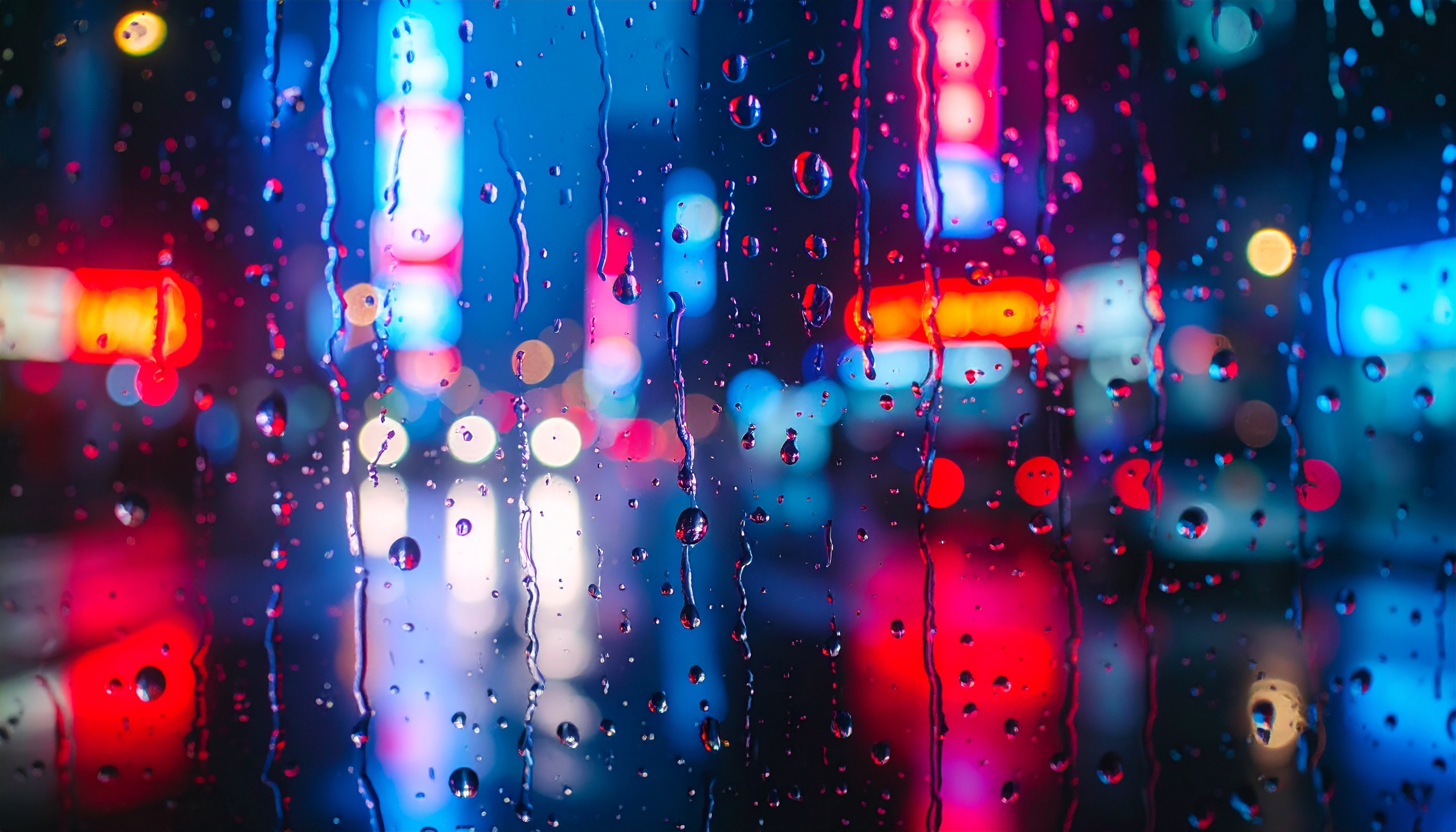 Vidro de janela com gotas de chuva focadas em primeiro plano, enquanto luzes de neon desfocadas criam um vibrante fundo urbano de cores azul e vermelha, transmitindo uma atmosfera noturna e moderna.