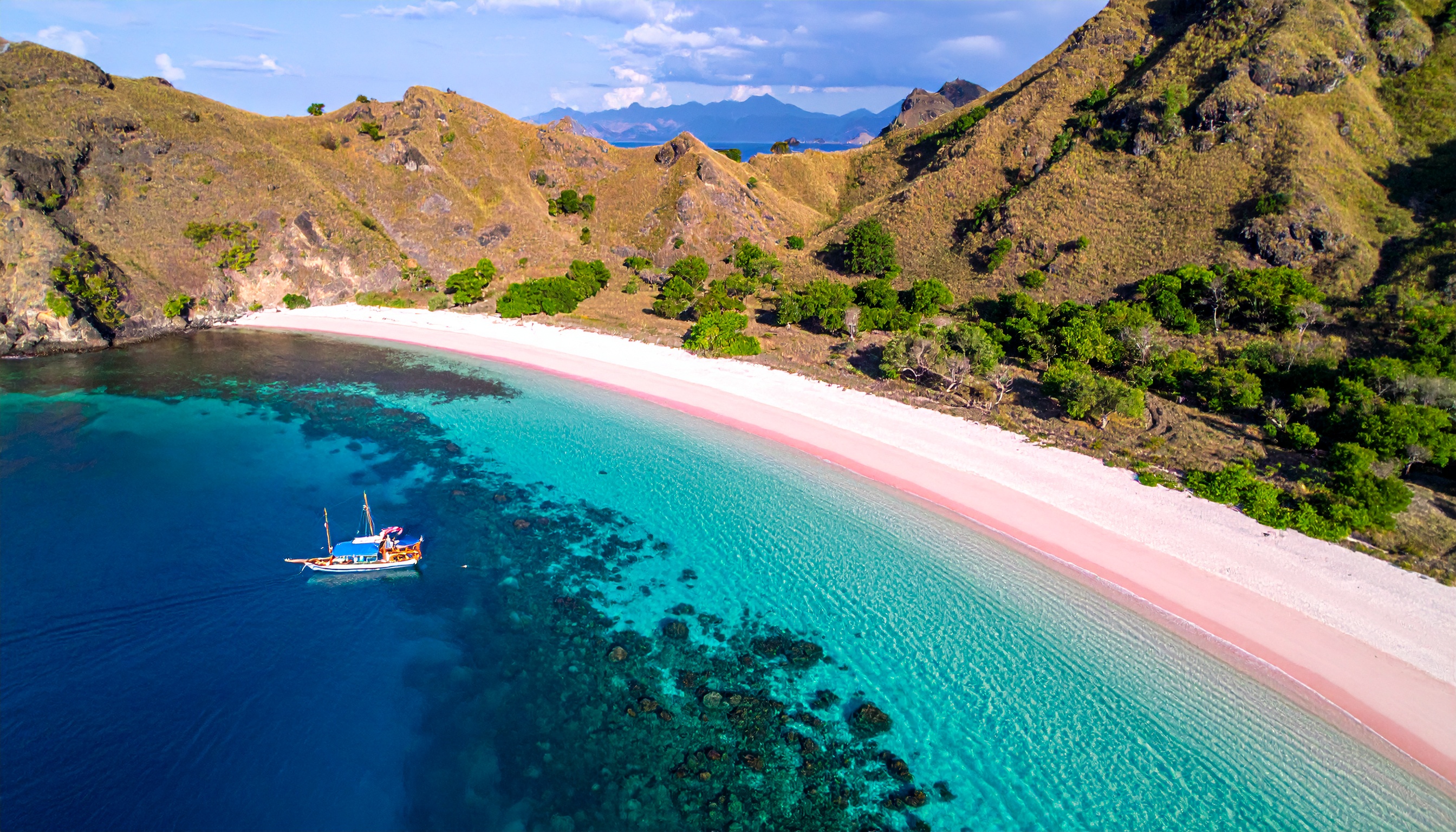 Praia isolada com areia rosada e águas cristalinas, ideal para relaxamento e turismo natural. Este cenário de praia paradisíaca oferece um refúgio perfeito longe do agito urbano. As águas azuis e as colinas verdes circundantes criam um contraste visual deslumbrante. Perfeito para uma escapadela romântica ou férias em família. A beleza única da areia rosada é um grande diferencial para amantes da natureza.