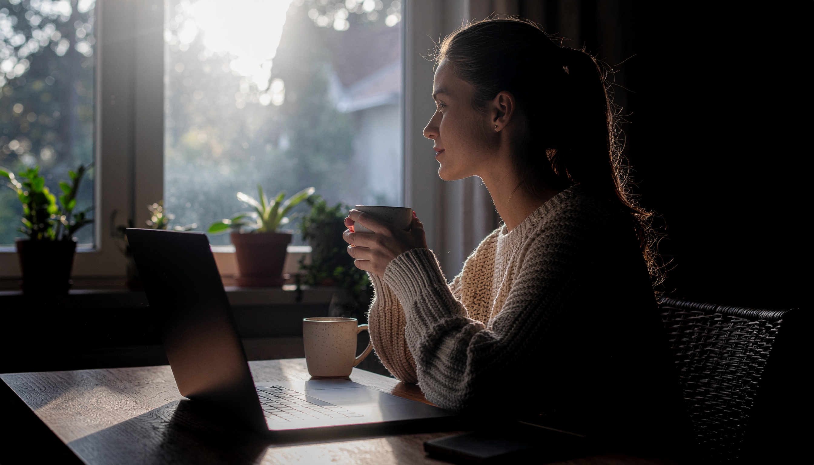 Woman Sitting at Wooden Table with Laptop and Cup