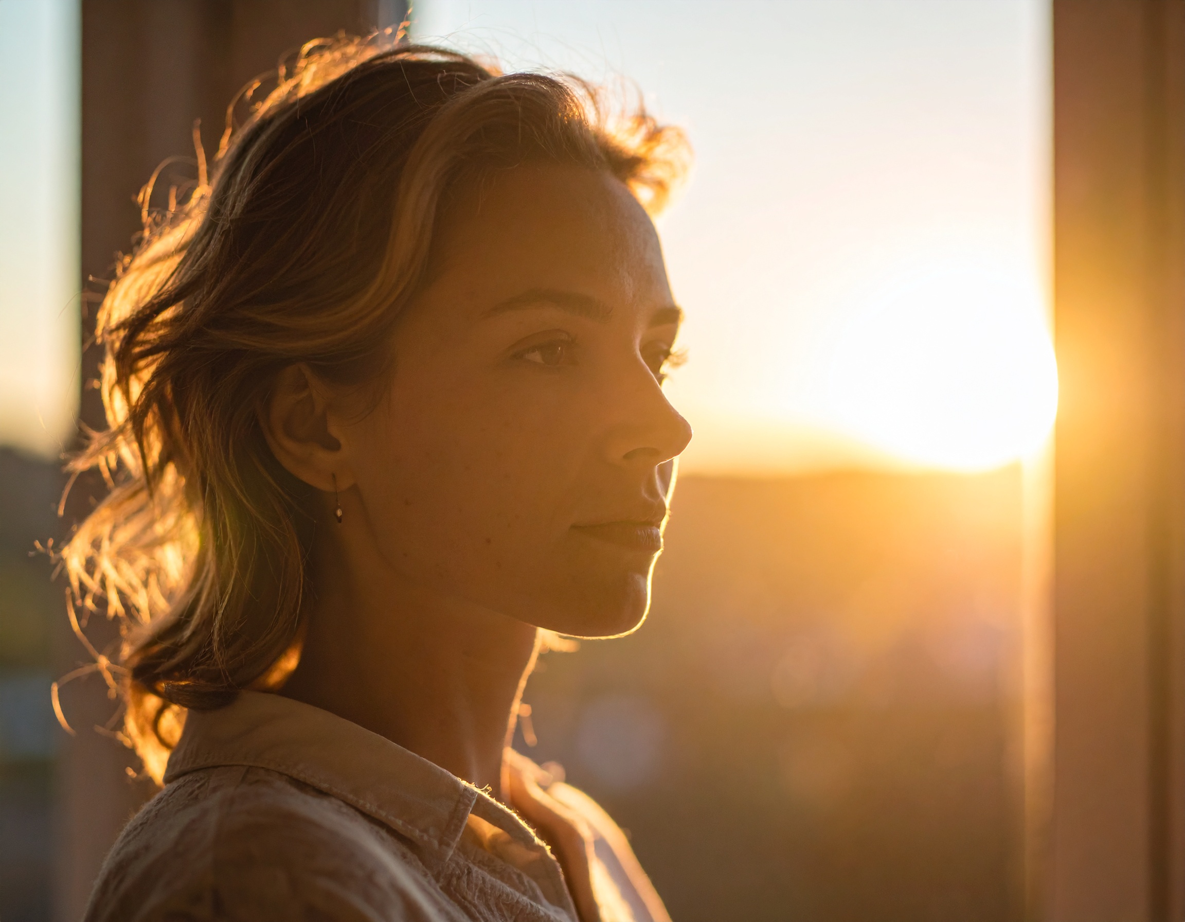 A woman with wavy hair is bathed in warm, golden sunlight streaming through a window