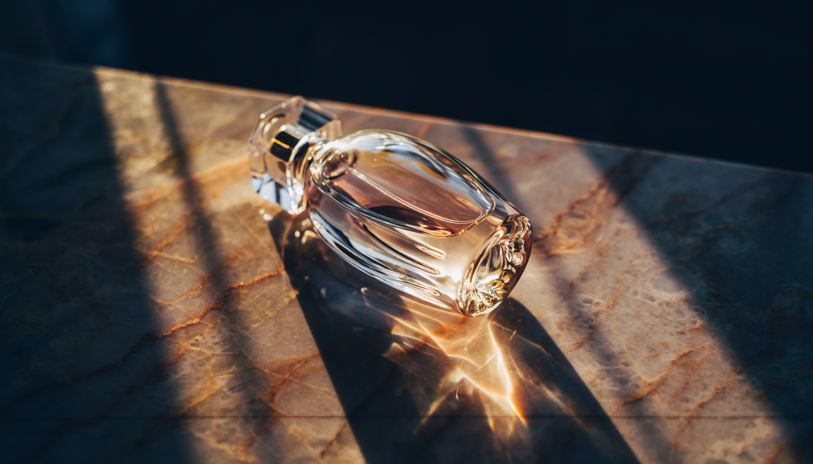 Frasco de perfume elegante repousa sobre uma superfície de mármore iluminada pela luz dourada do sol, criando reflexos cintilantes e atmosfera luxuosa.