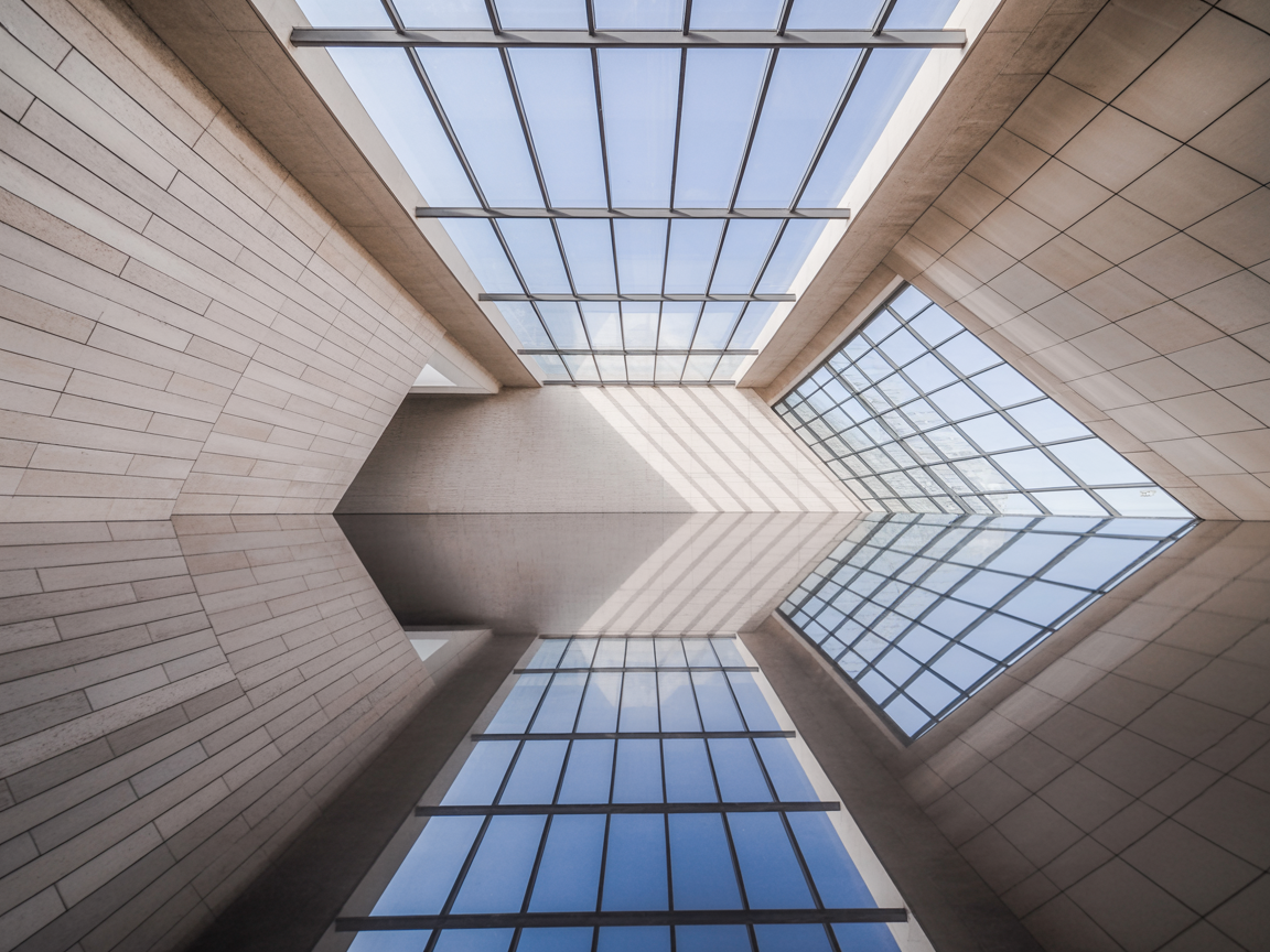A modern architectural ceiling features large glass panels framed by sleek, light stone