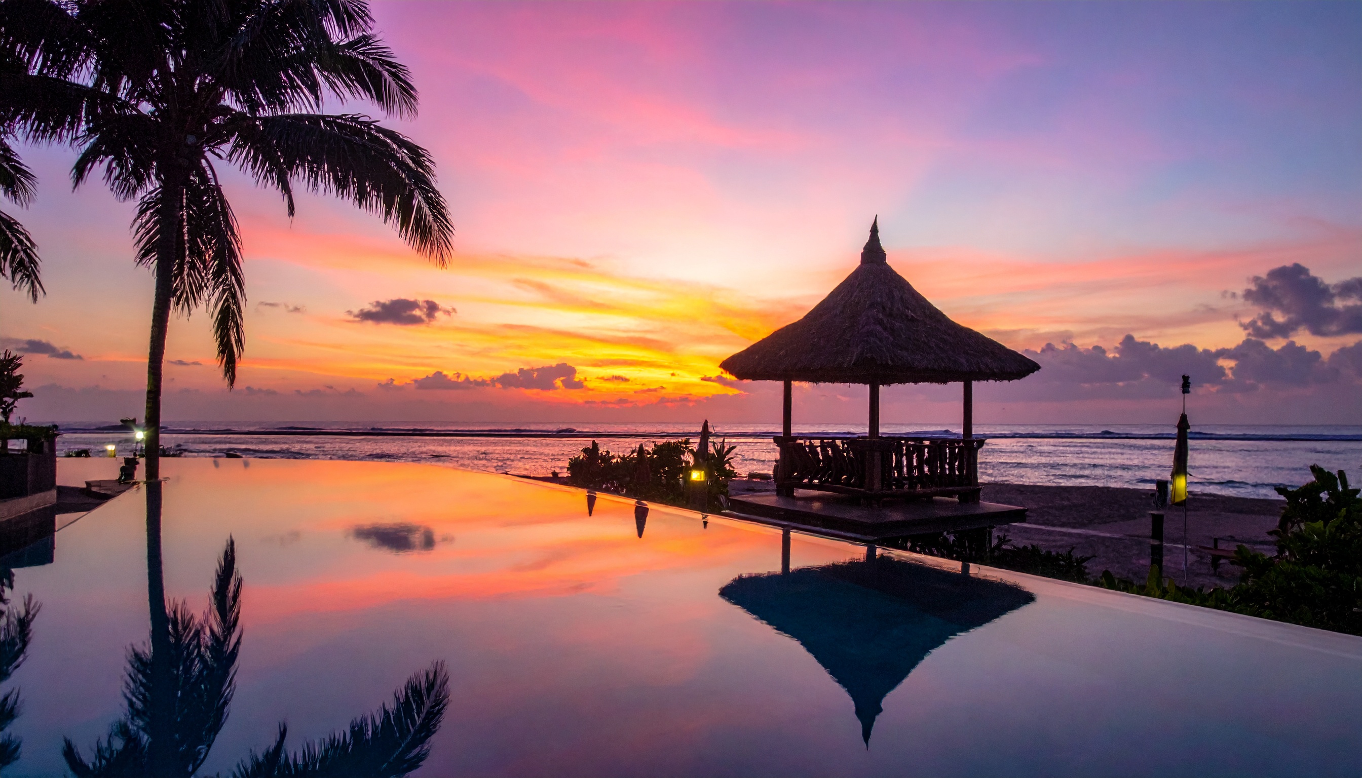 A serene tropical beach scene at sunset with palm trees and a thatched gazebo