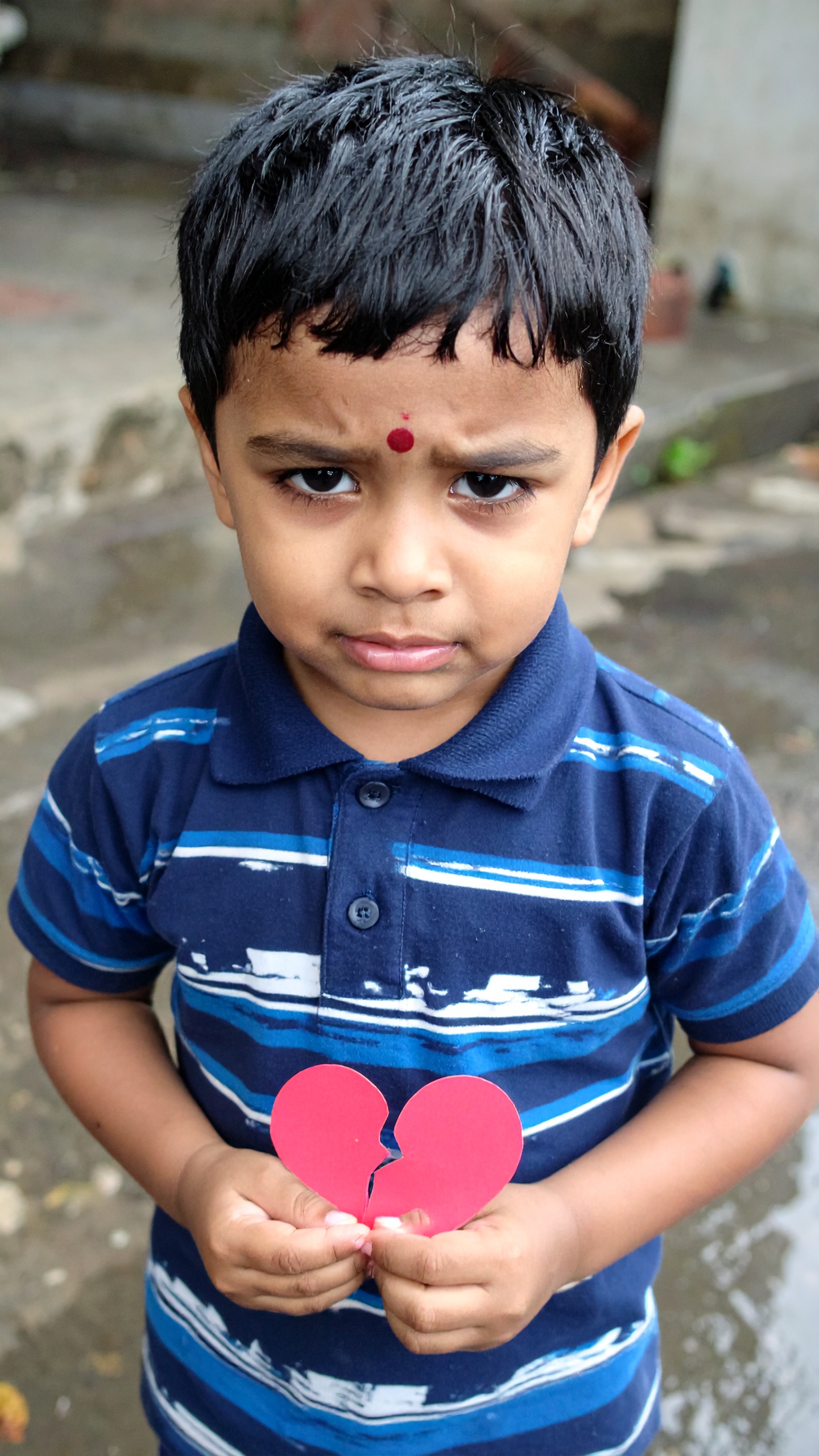 A young boy holds a red, broken heart-shaped paper with a serious expression