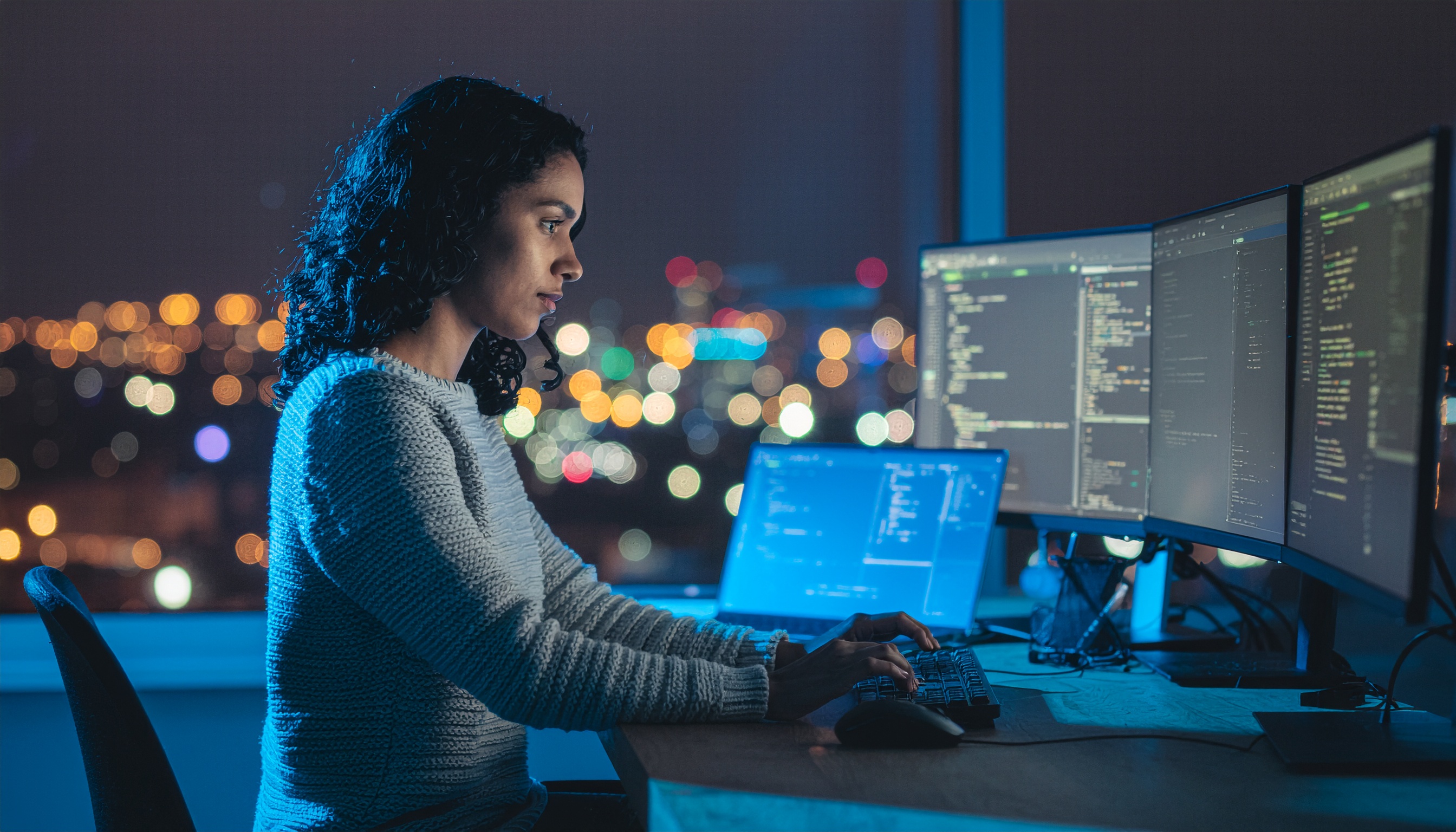 Mulher programadora trabalhando à noite em um escritório, com múltiplas telas de código, em ambiente urbano iluminado. A atmosfera é de foco e concentração, destacando a dedicação no desenvolvimento de software.