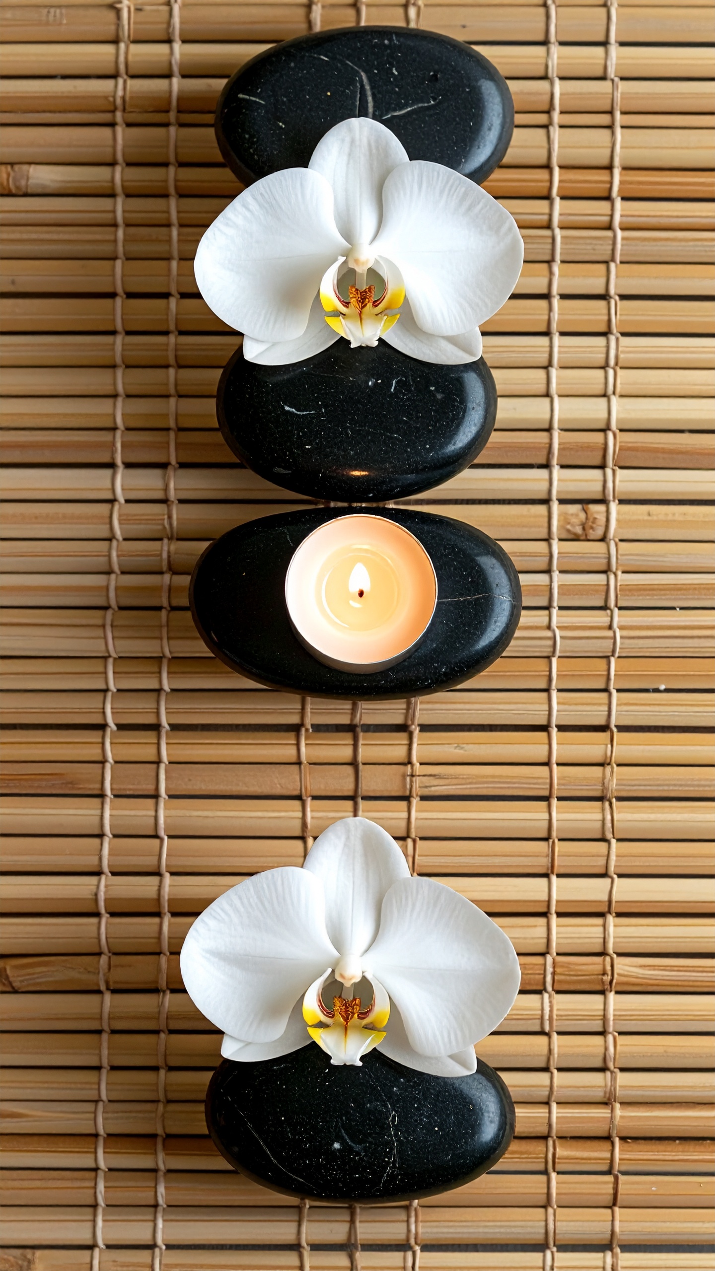 White orchids and a candle rest on smooth black stones atop a bamboo mat