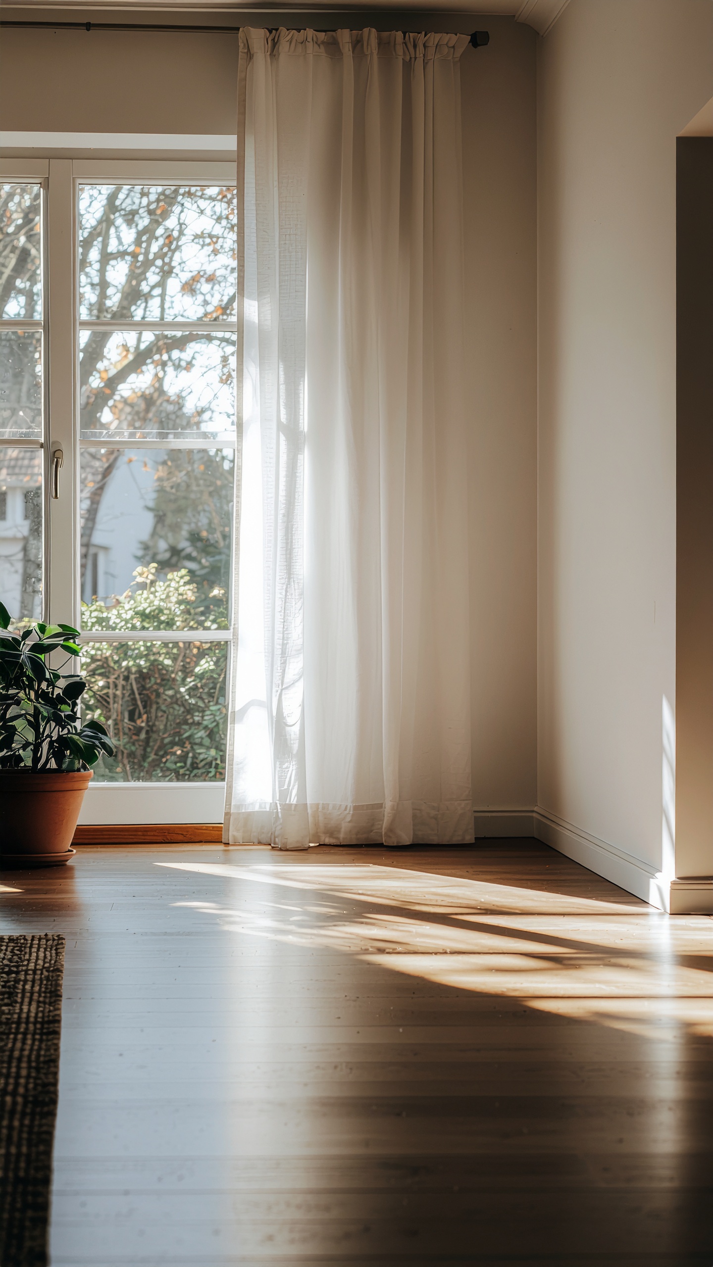 Sunlight streams through sheer white curtains onto a wooden floor in a serene living room