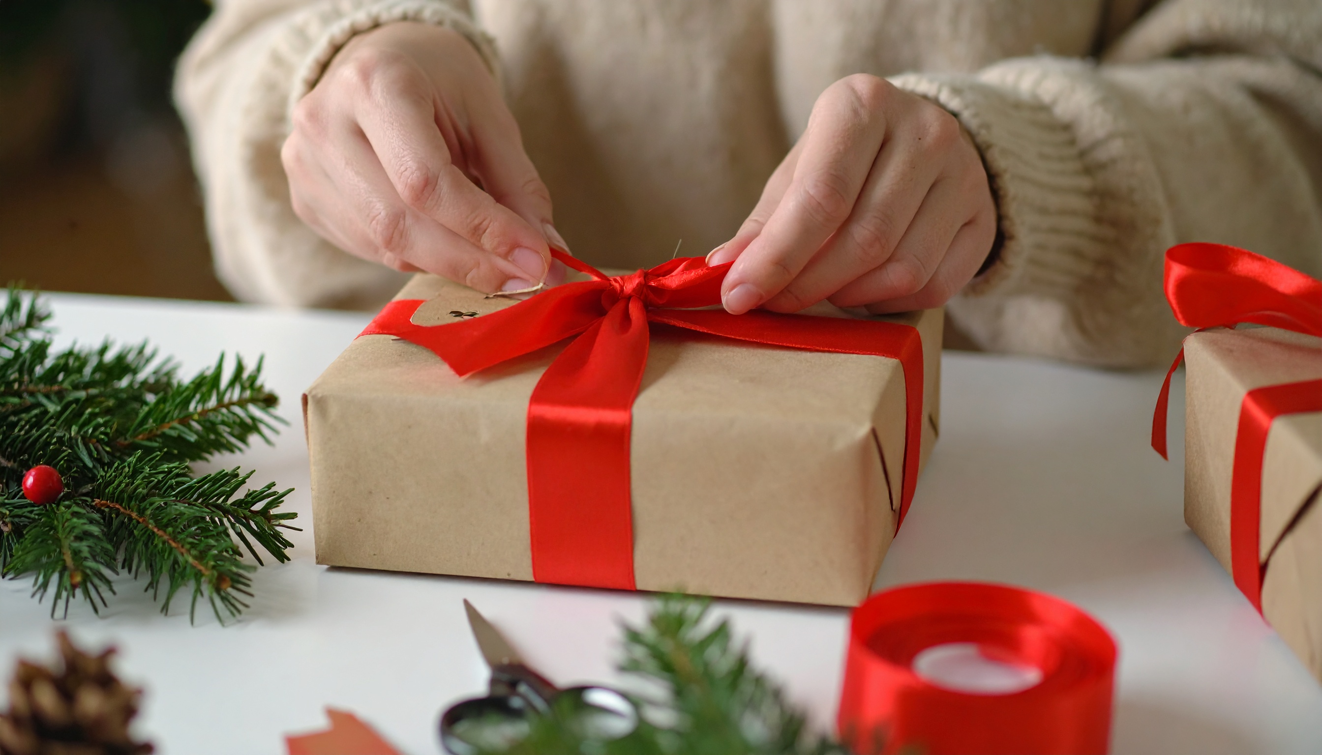 Hands Wrapping Gift with Kraft Paper and Red Ribbon