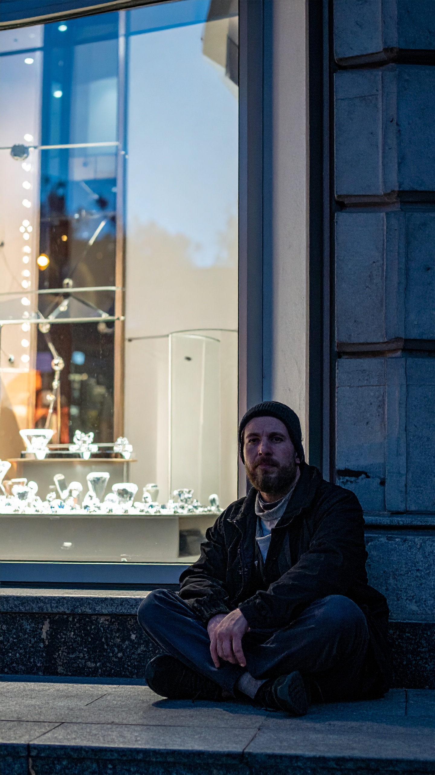A man sits outside a brightly lit jewelry store