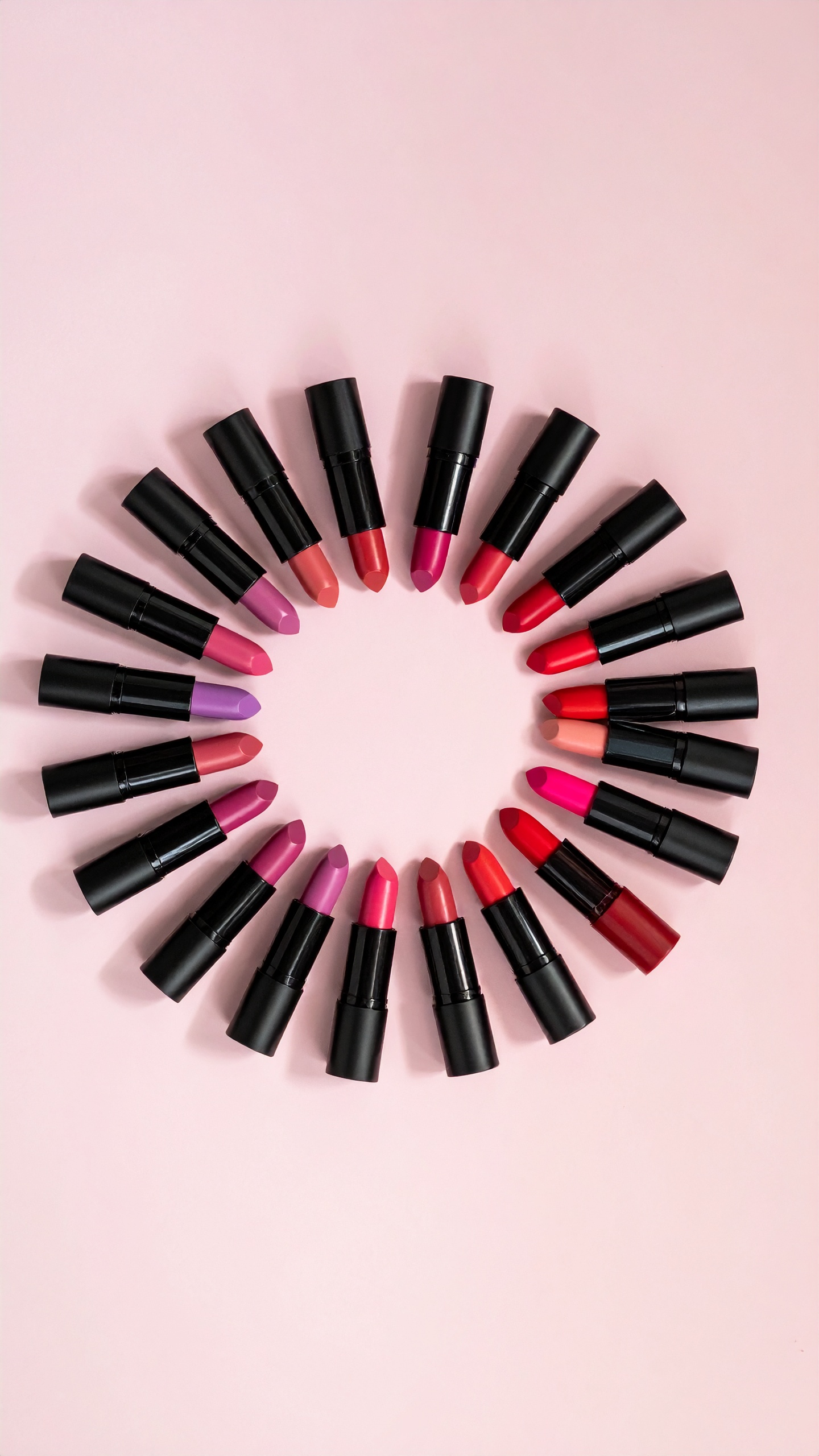 A circle of vibrant lipsticks arranged on a soft pink background offers a colorful display