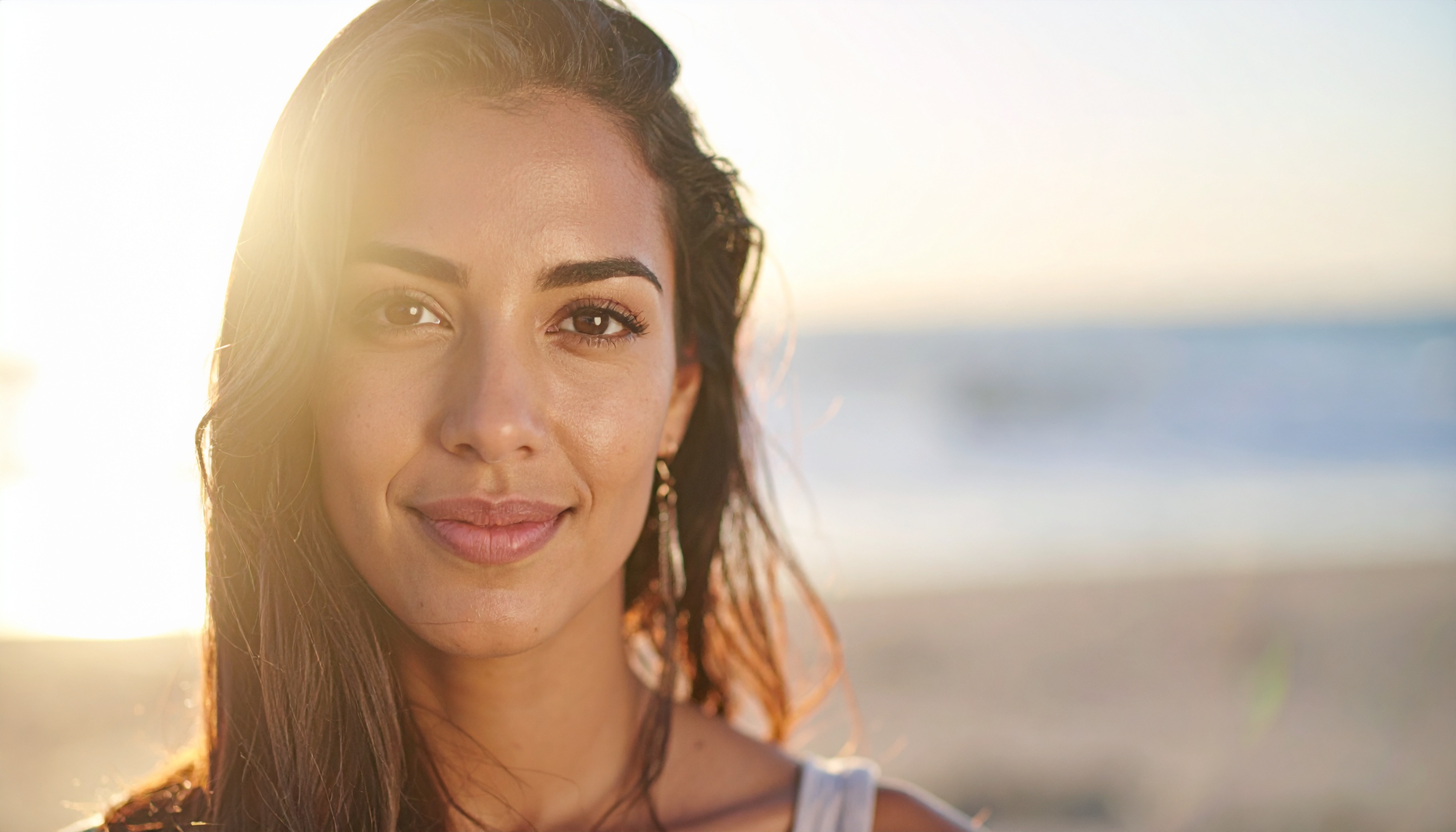 A woman stands on a sunlit beach with a serene expression