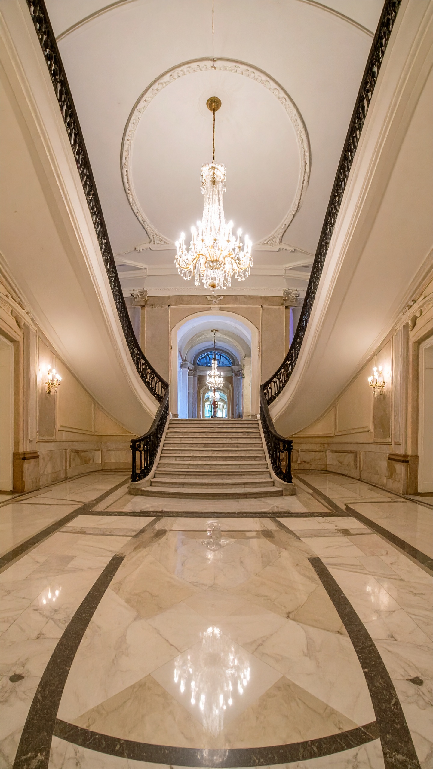 A grand marble staircase with an opulent chandelier creates a luxurious atmosphere