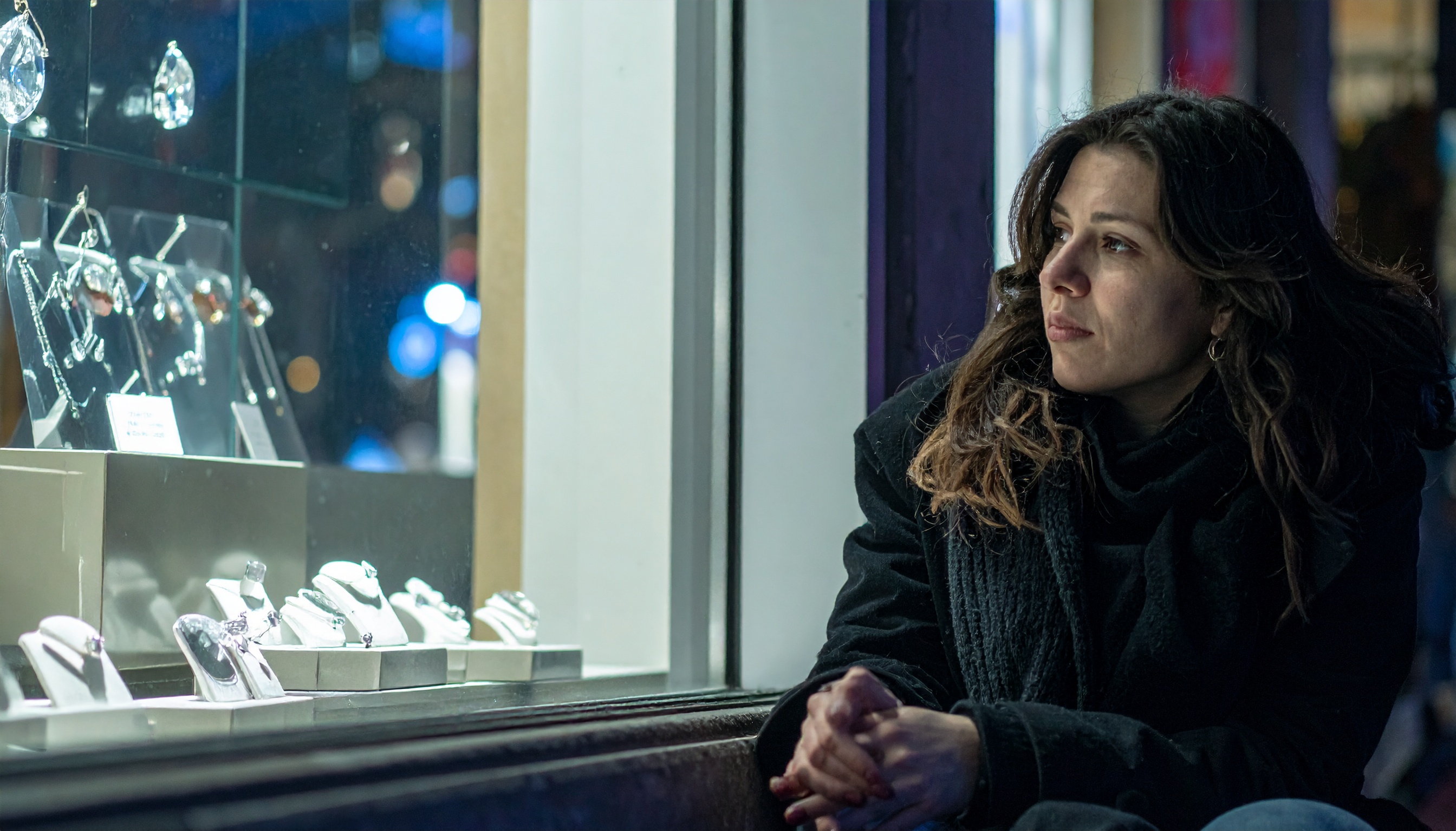A woman gazes thoughtfully at a jewelry store window, highlighting the allure of luxury accessories