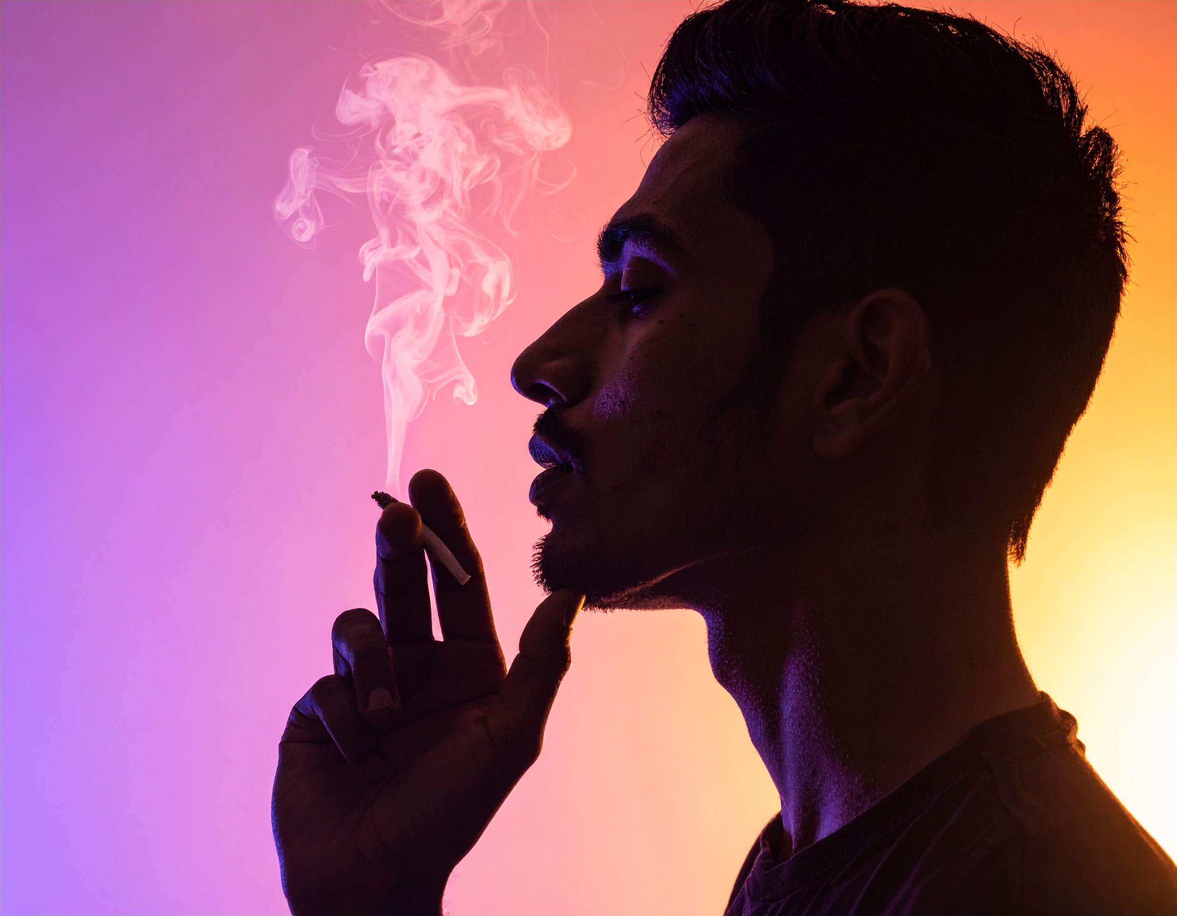 A profile silhouette of a person exhaling smoke against a vibrant gradient background