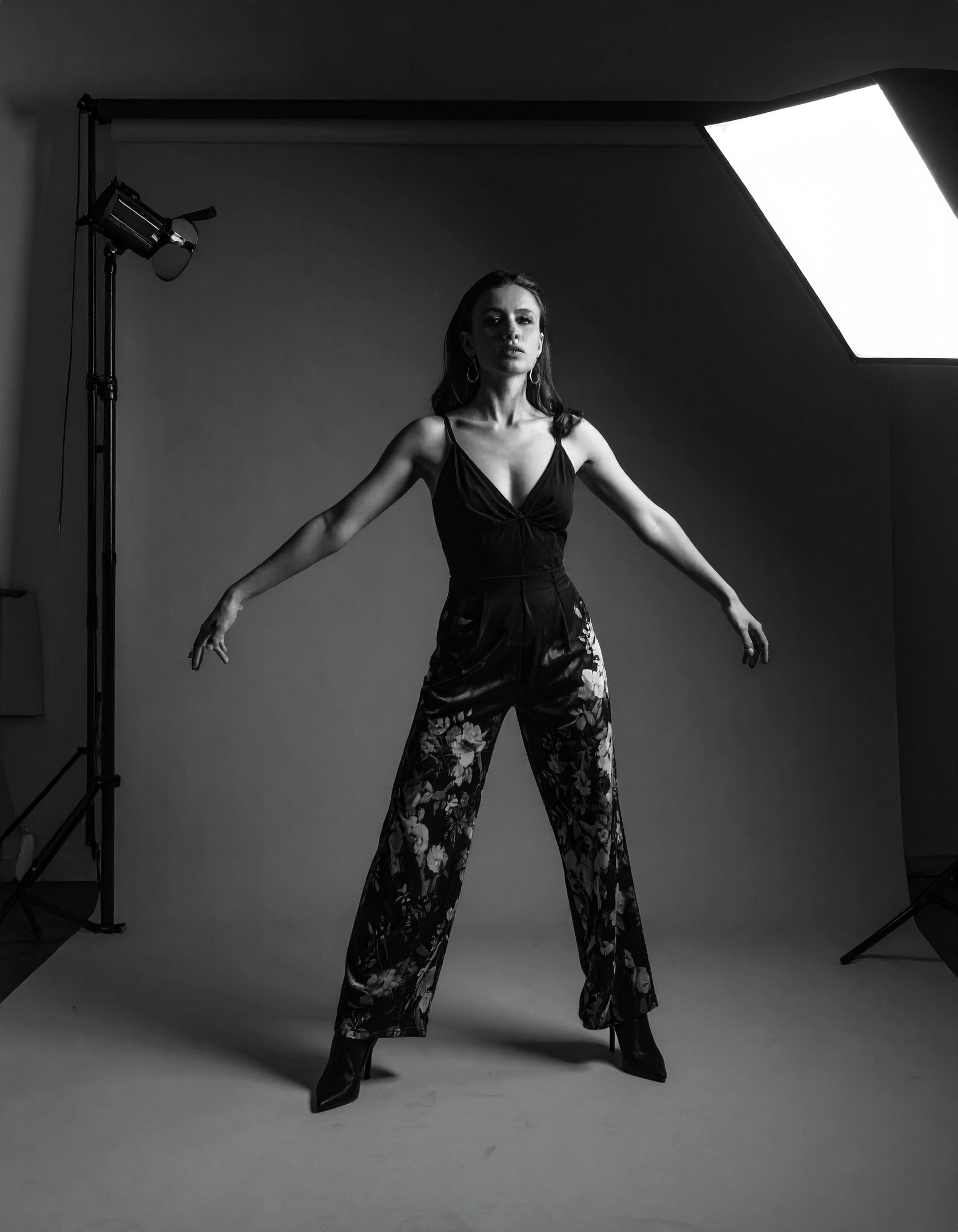 A woman poses confidently in a photography studio, dressed in stylish floral pants and a black top