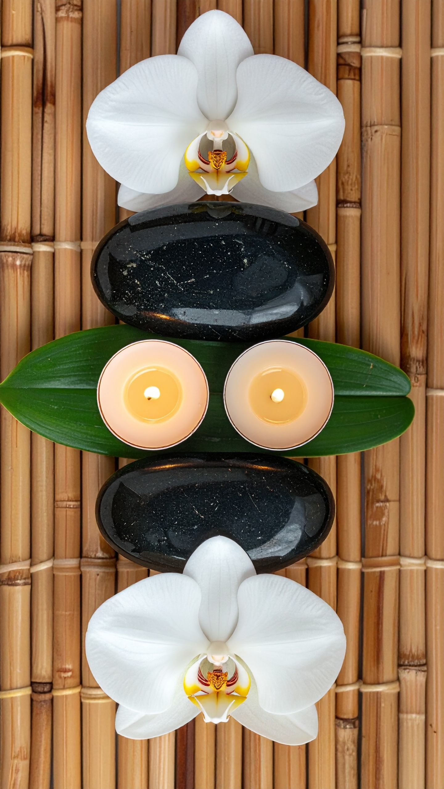 A tranquil spa arrangement features smooth black stones, white orchids, and calming candles on a