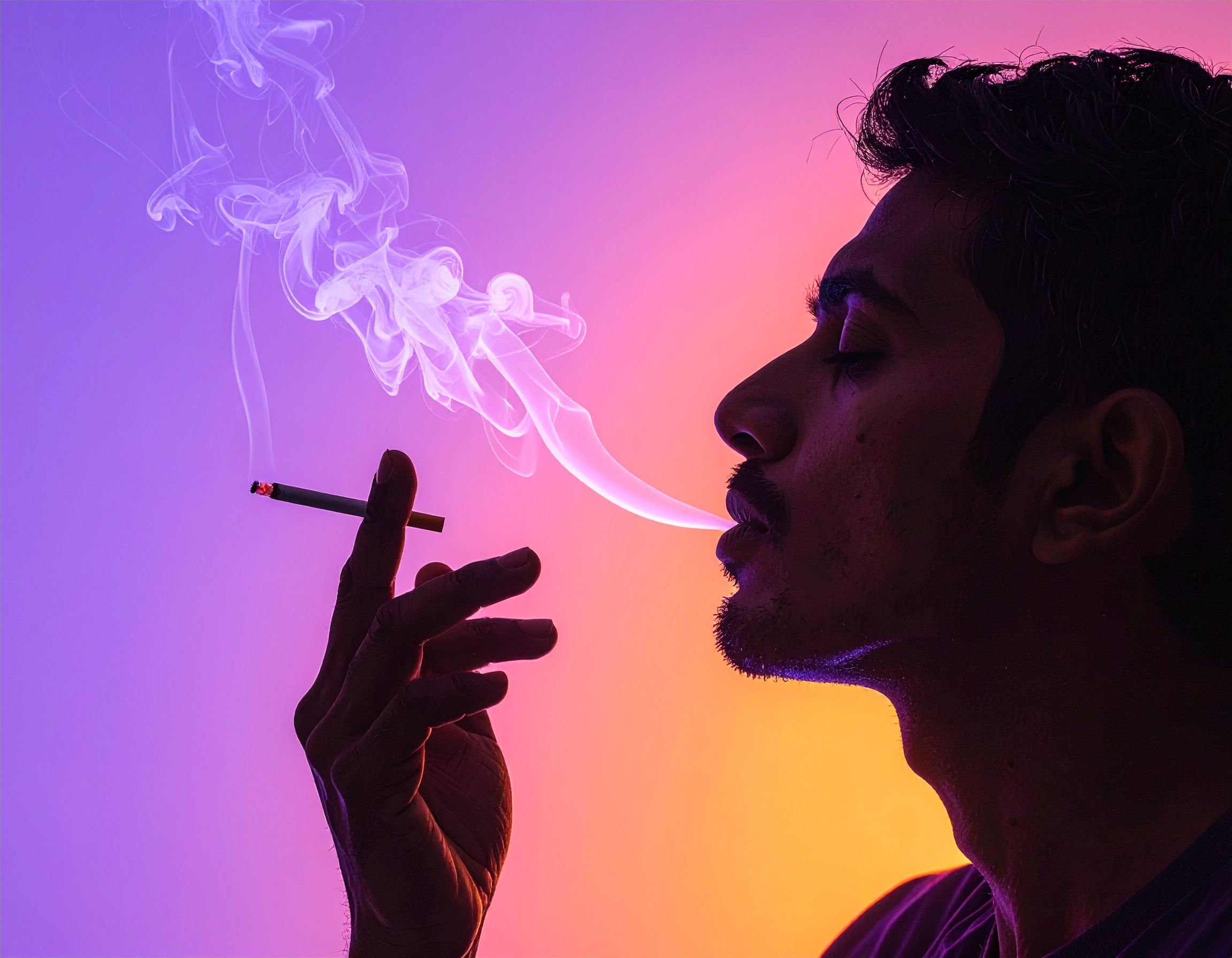 A man exhales smoke against a vibrant gradient background
