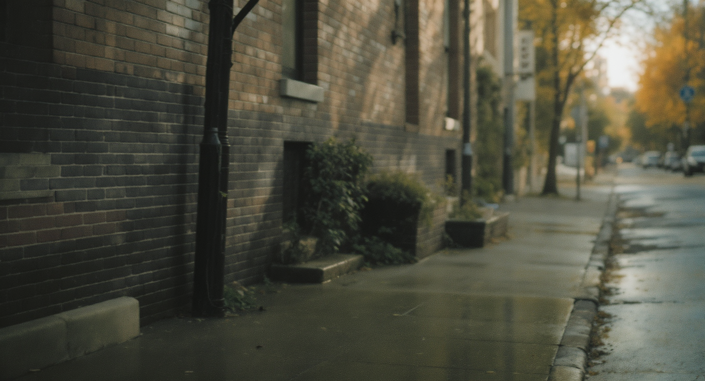 Rua urbana deserta com calçada molhada ao lado de prédio de tijolos. Ideal para cenários de marketing que buscam transmitir tranquilidade e isolamento. O tijolo vermelho, combinado com a iluminação suave, cria uma atmosfera serena e nostálgica. Perfeita para campanhas publicitárias de outono ou inverno, quando se quer realçar a sensação de calma. O contraste entre a textura do tijolo e a umidade da calçada adiciona profundidade visual.