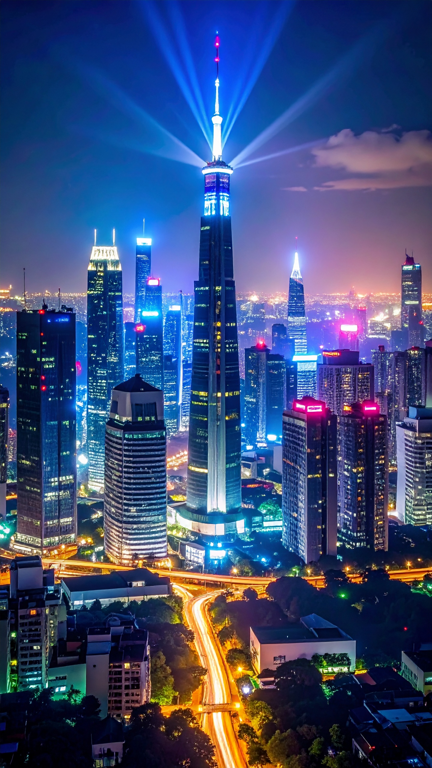 Horizonte urbano iluminado à noite com arranha-céus e luzes vibrantes. Ideal para transmitir modernidade e inovação em projetos visuais. O destaque é uma torre central com luzes azuis e brancas que se sobressaem no centro da cena. Perfeito para campanhas publicitárias que buscam evocar um ambiente metropolitano e tecnológico. A imagem oferece um contraste dramático entre as luzes artificiais e o céu noturno, criando um efeito visual impressionante.