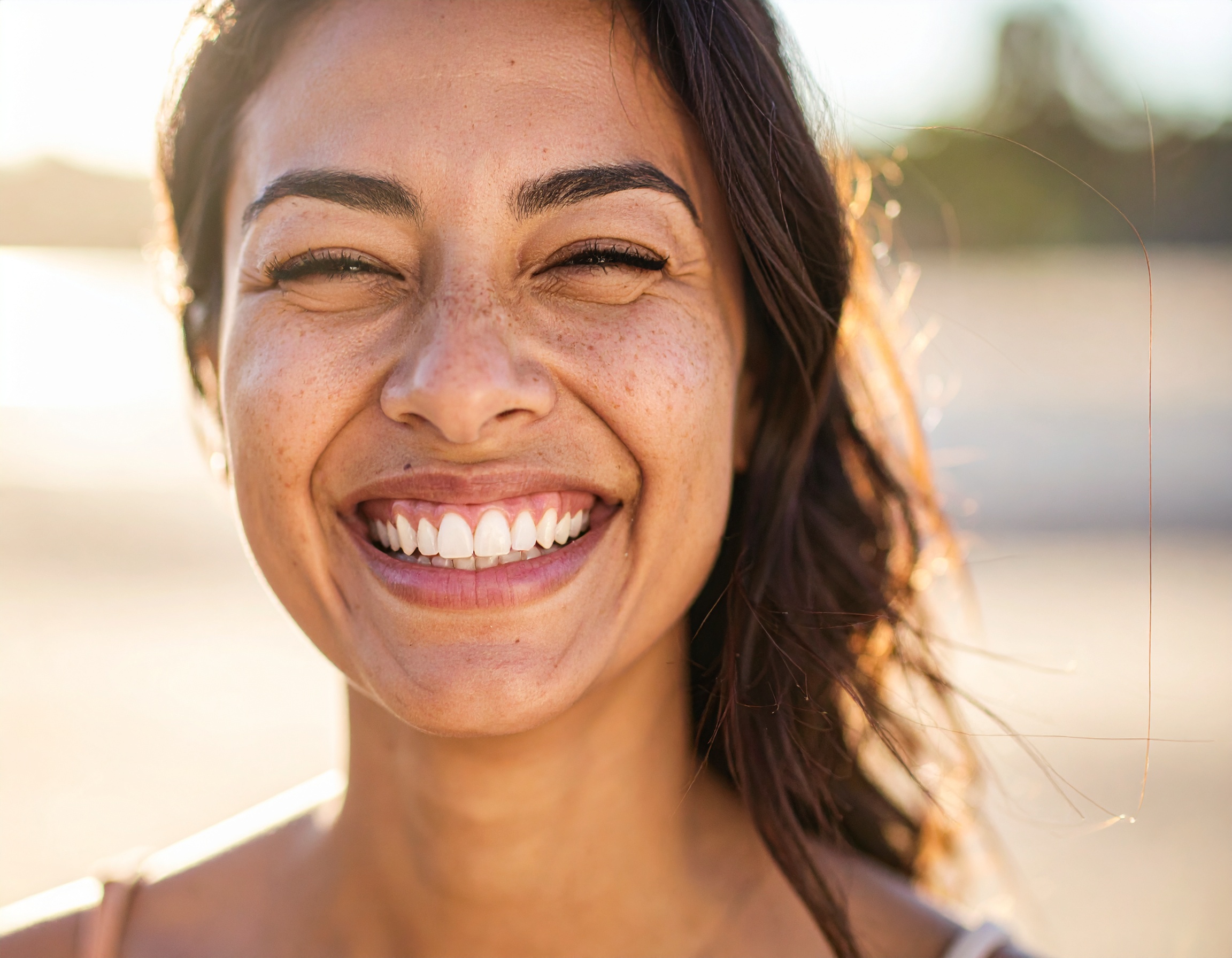 A joyful woman is smiling brightly in a sunny outdoor setting