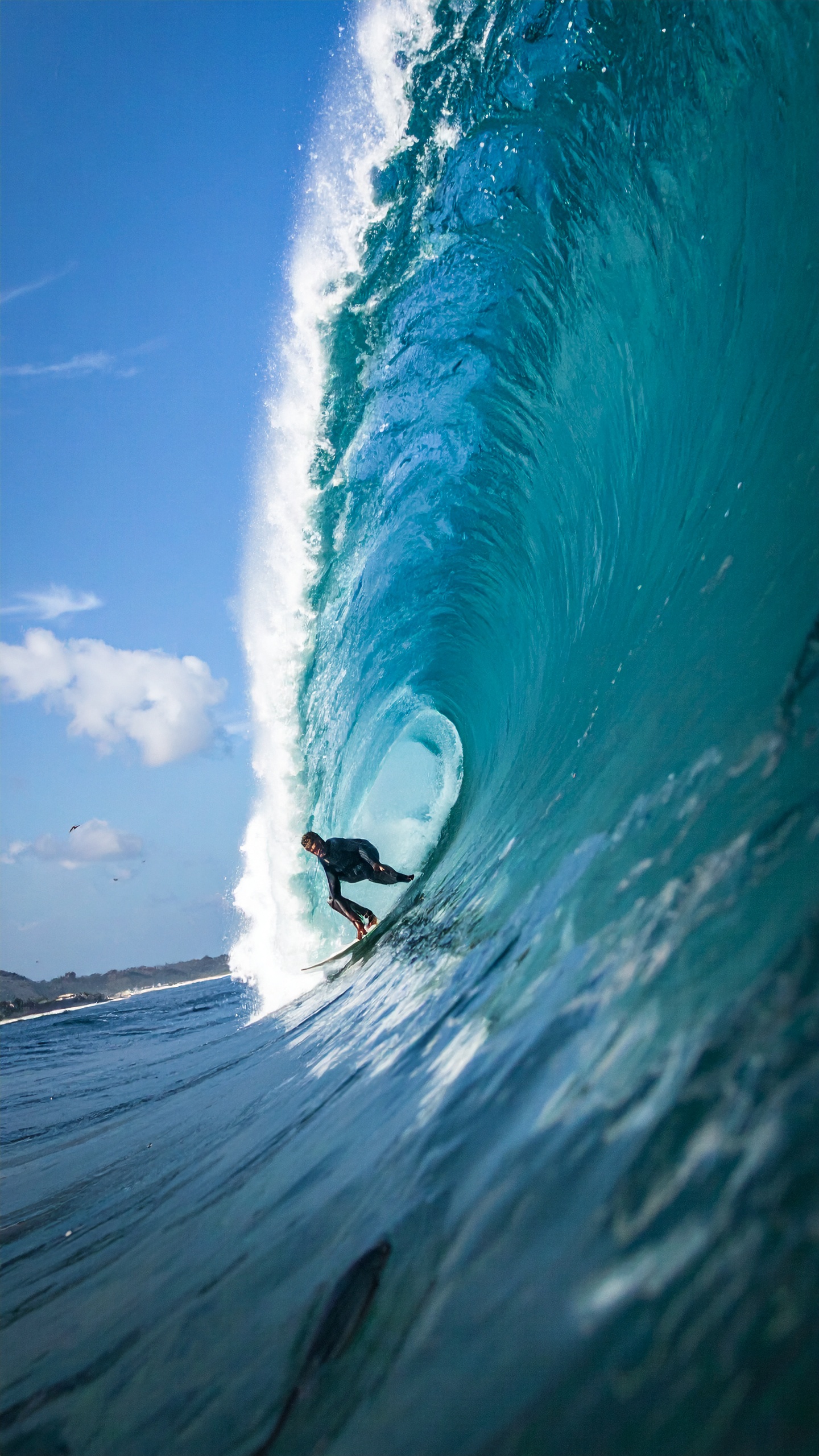 A surfer skillfully navigates a towering blue wave under a clear sky