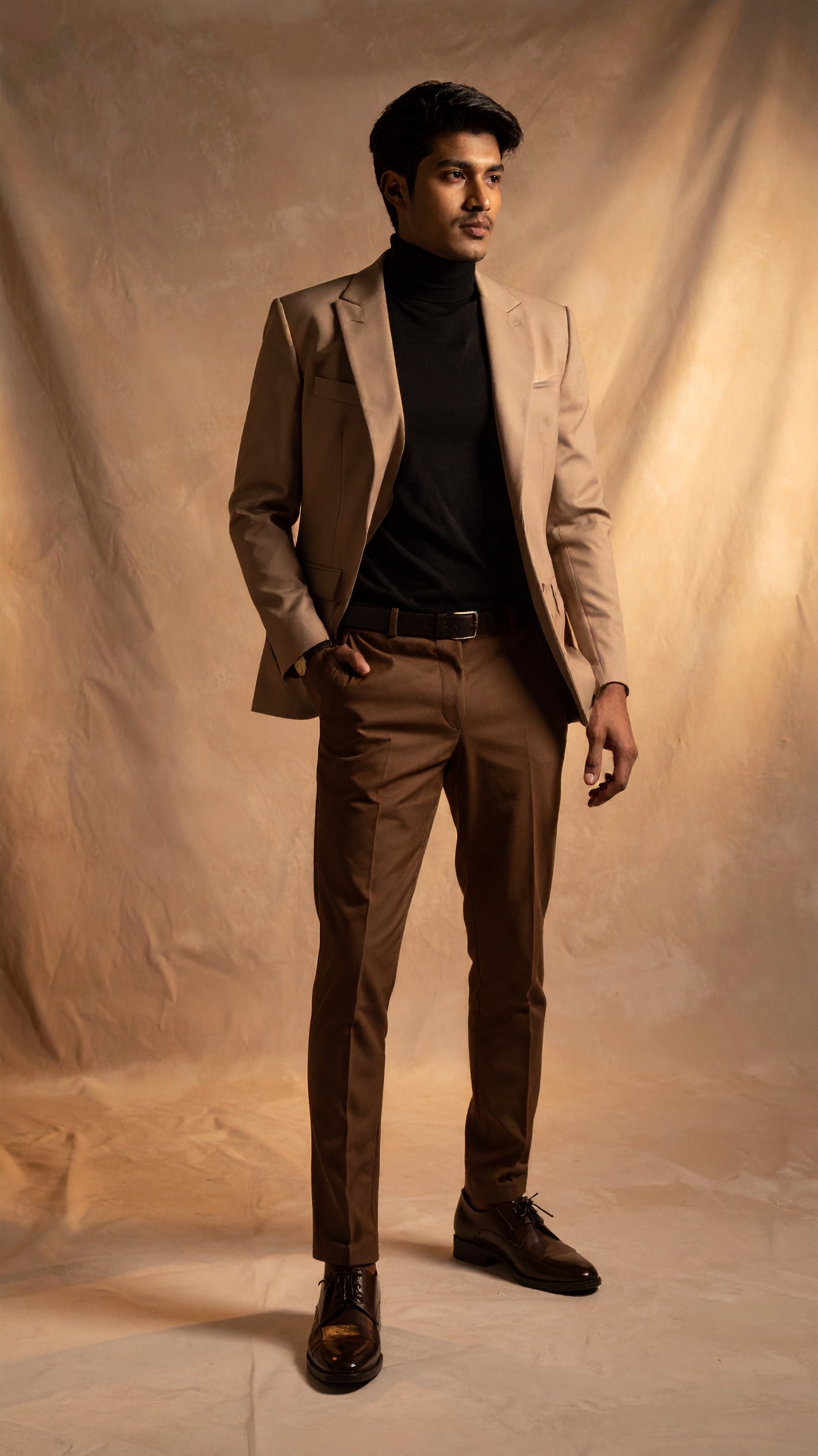 A man in a tailored beige suit stands confidently against a neutral backdrop