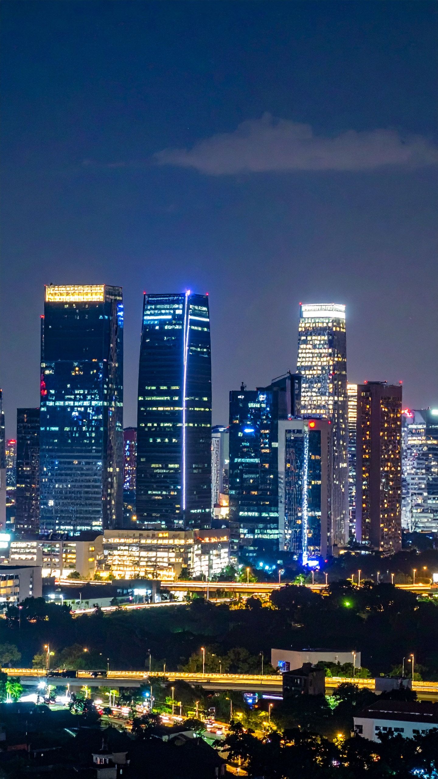 Arranha-céus iluminados compõem uma vibrante paisagem urbana noturna. Ideal para representar modernidade e dinamismo em materiais promocionais. As luzes dos edifícios contrastam com o céu escuro, destacando a arquitetura. Perfeita para campanhas publicitárias de negócios ou tecnologia em ambientes urbanos. A imagem captura a energia e o movimento de uma metrópole ativa.