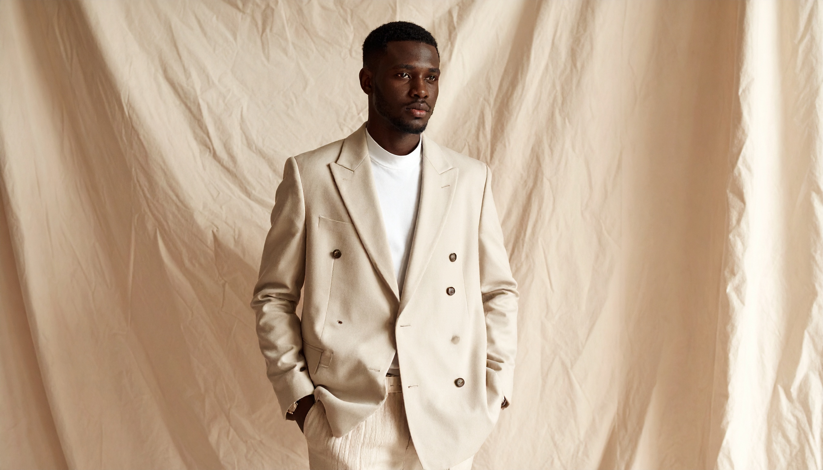 A man stands confidently in a stylish beige double-breasted suit