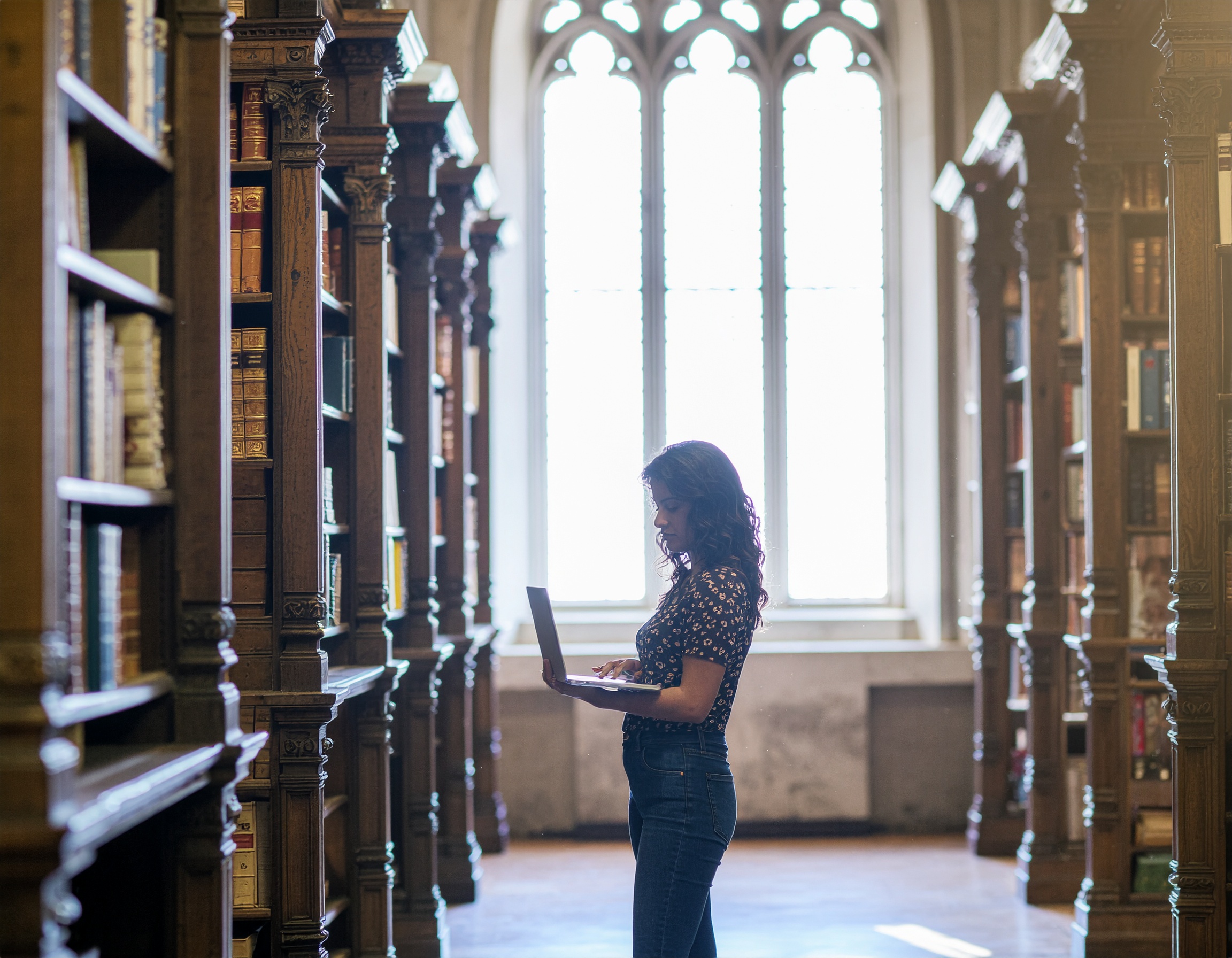 Woman Using Laptop in Historic Library with Stained Glass