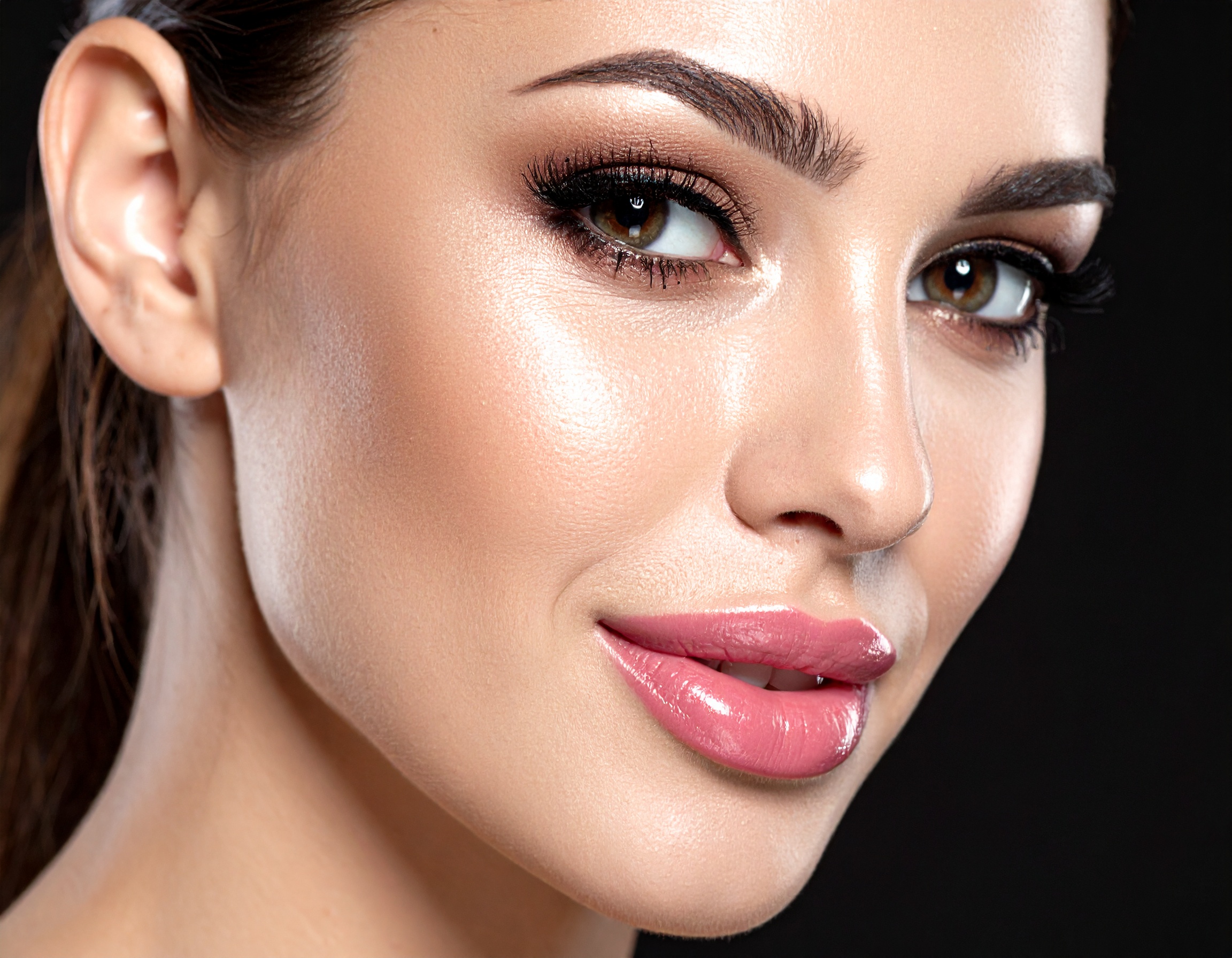 Close-up of a woman with flawless makeup, highlighting her glowing skin and perfect eyeliner