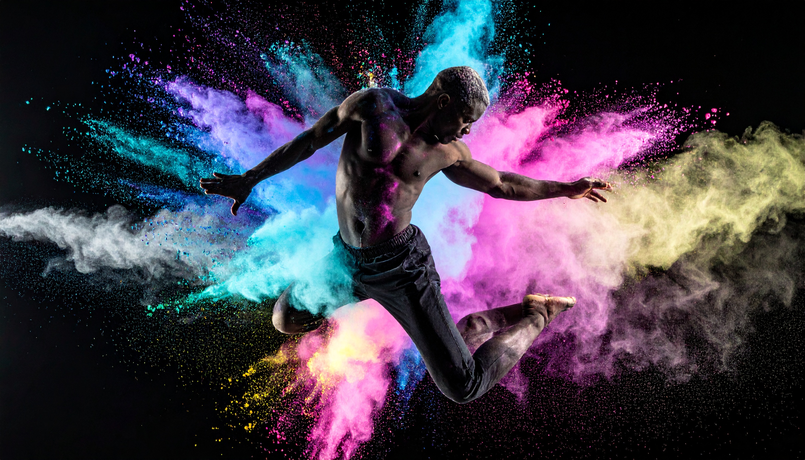 A dynamic dancer leaps amidst a burst of vibrant colored powders