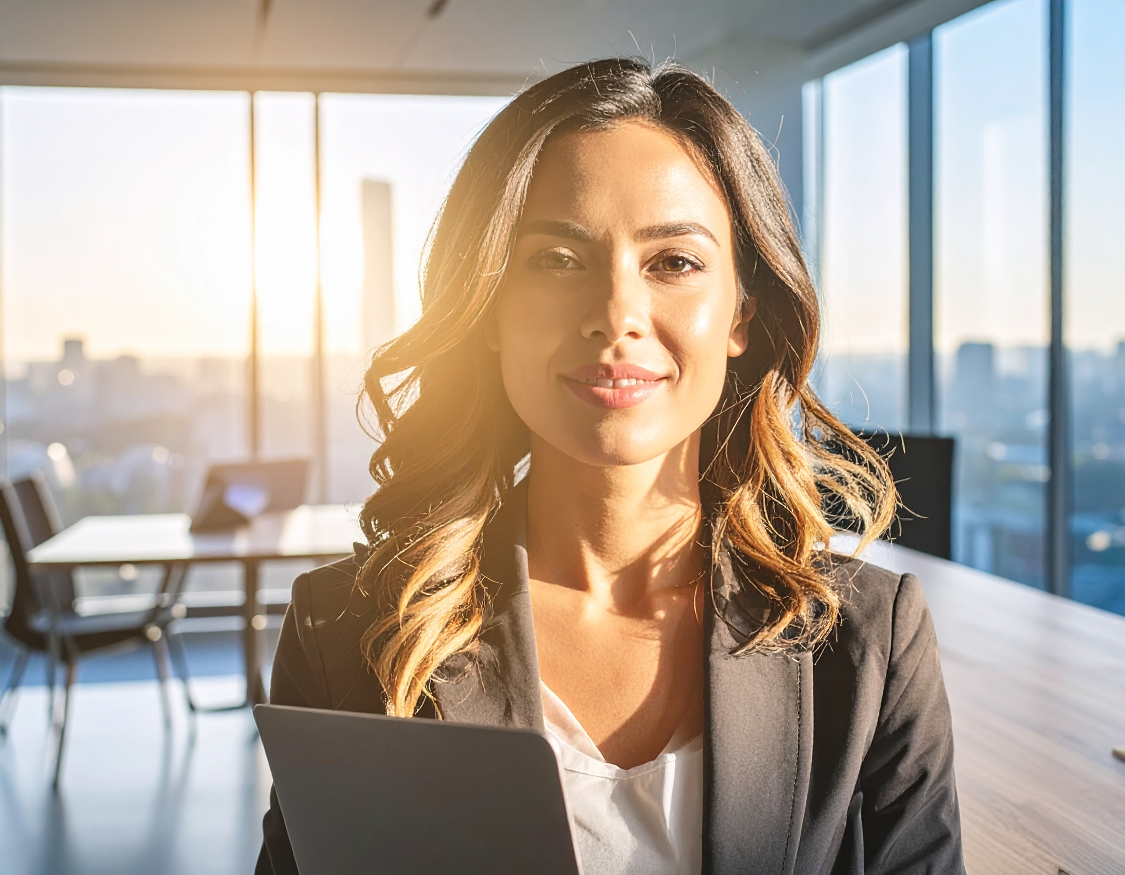 Mulher sorridente em sala de reuniões iluminada por sol poente em escritório moderno com vista panorâmica da cidade, transmitindo confiança e profissionalismo.