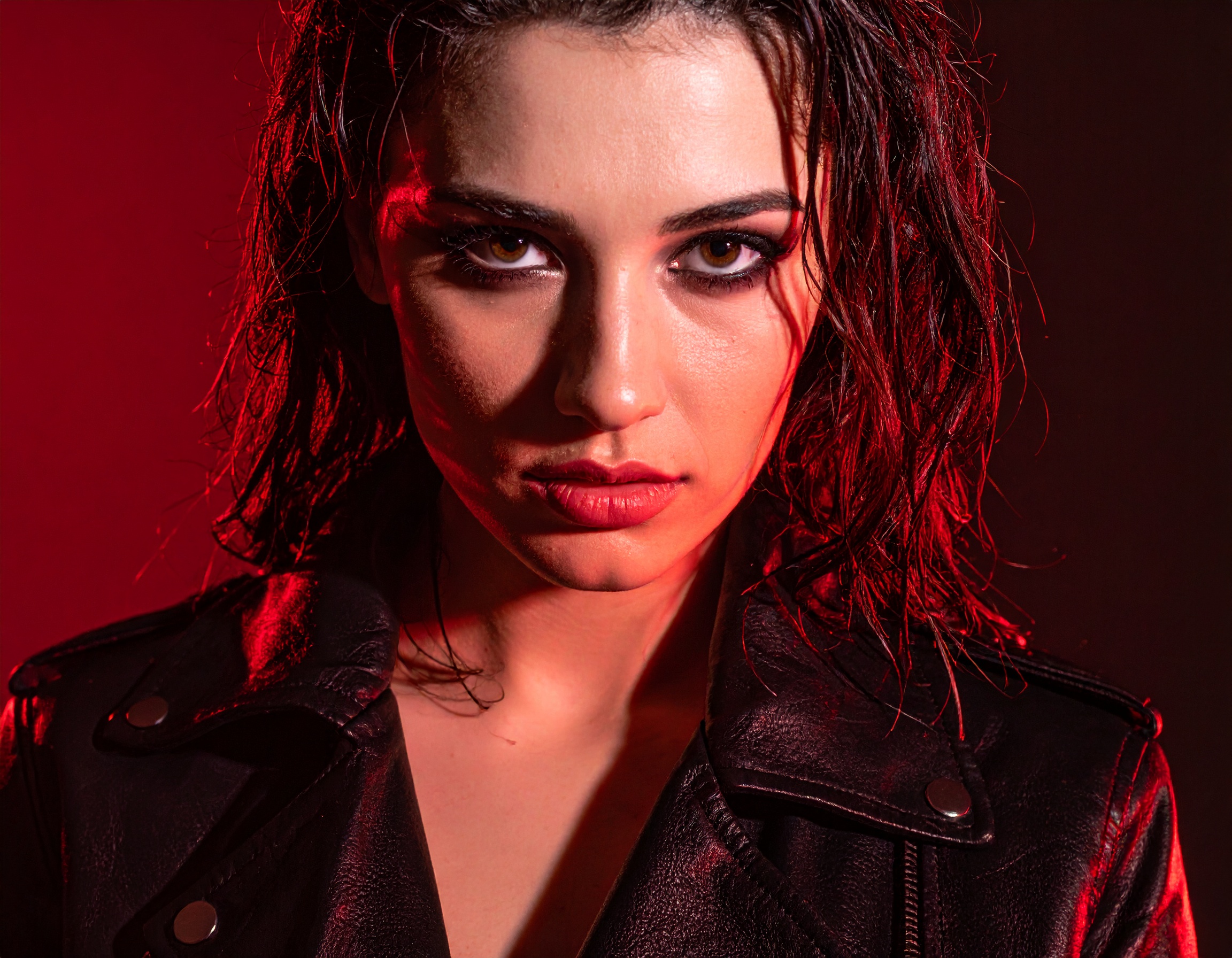 A woman with intense eyes and wet hair is highlighted in dramatic red lighting