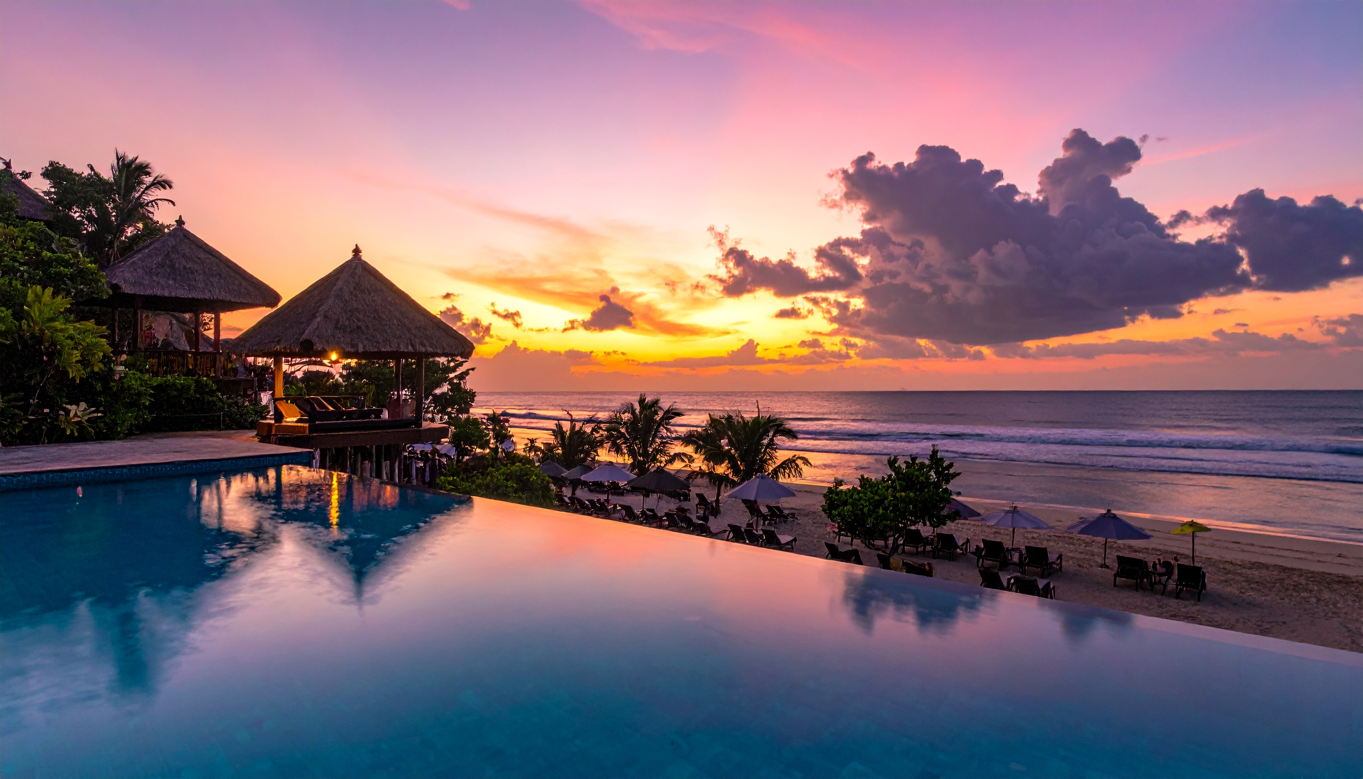Piscina de borda infinita com vista para um pôr do sol deslumbrante na praia. Ideal para resorts de luxo que buscam atrair visitantes em busca de relaxamento e beleza natural. As cores vibrantes do céu refletindo na água criam uma atmosfera serena e sofisticada. Ambientes como este são perfeitos para férias de verão ou retiros românticos. A combinação de natureza e arquitetura moderna oferece um cenário de tirar o fôlego.