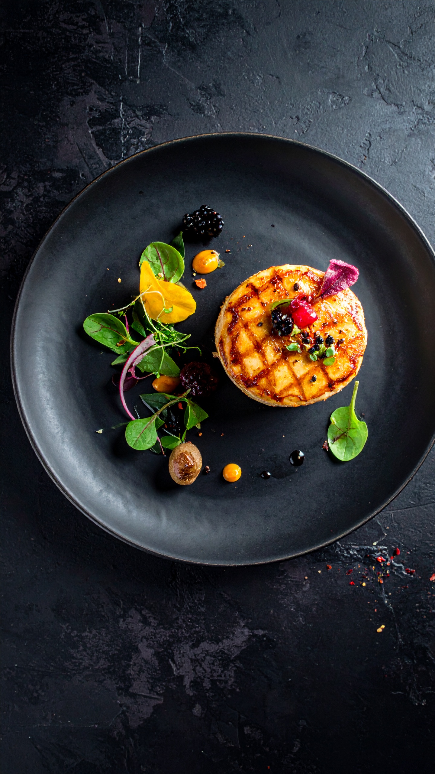 A beautifully plated gourmet dish sits on a dark ceramic plate