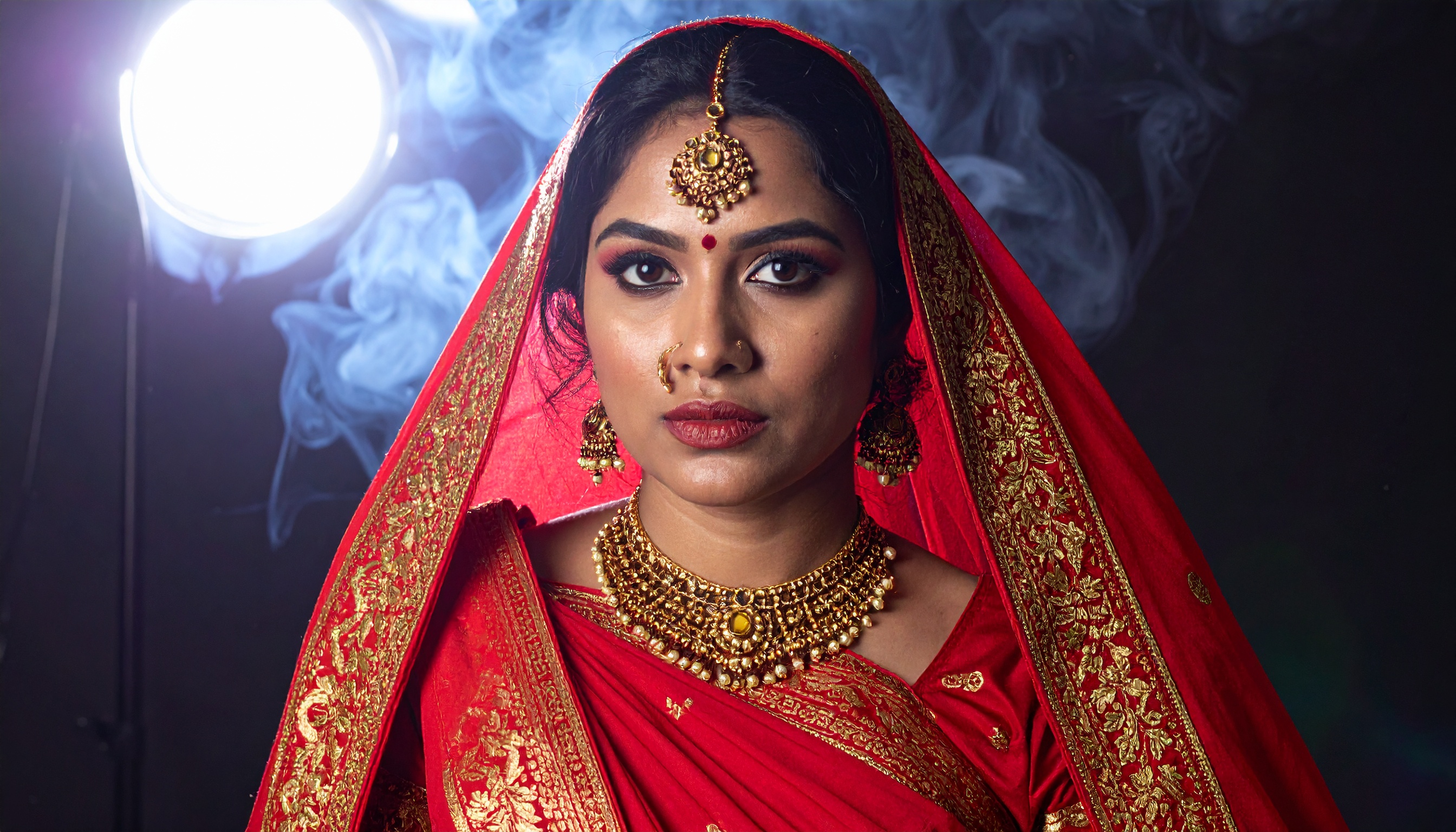 A woman in traditional bridal attire is adorned with intricate jewelry and a vibrant red sari