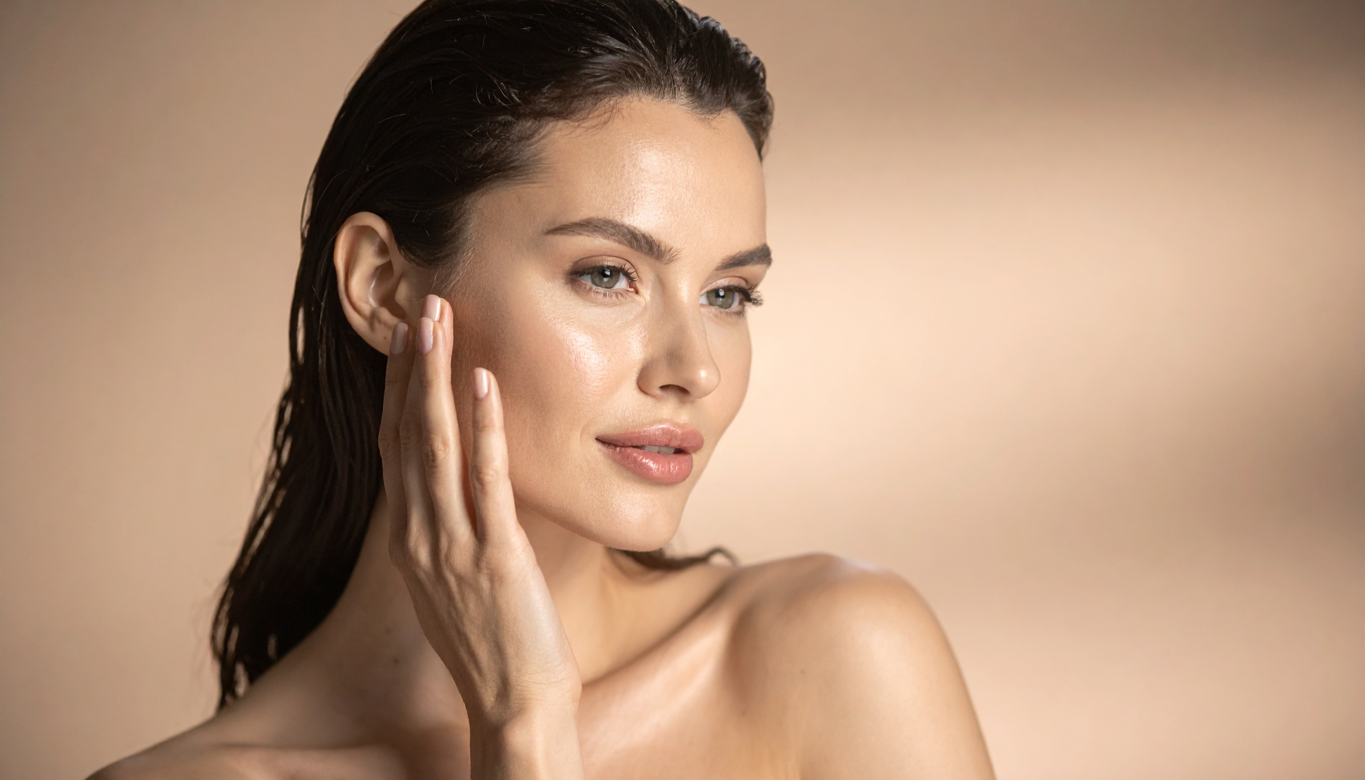 Retrato feminino em close-up com foco na pele saudável e radiante, em fundo bege minimalista. A expressão serena transmite elegância e confiança, ideal para campanhas de cuidados com a pele.