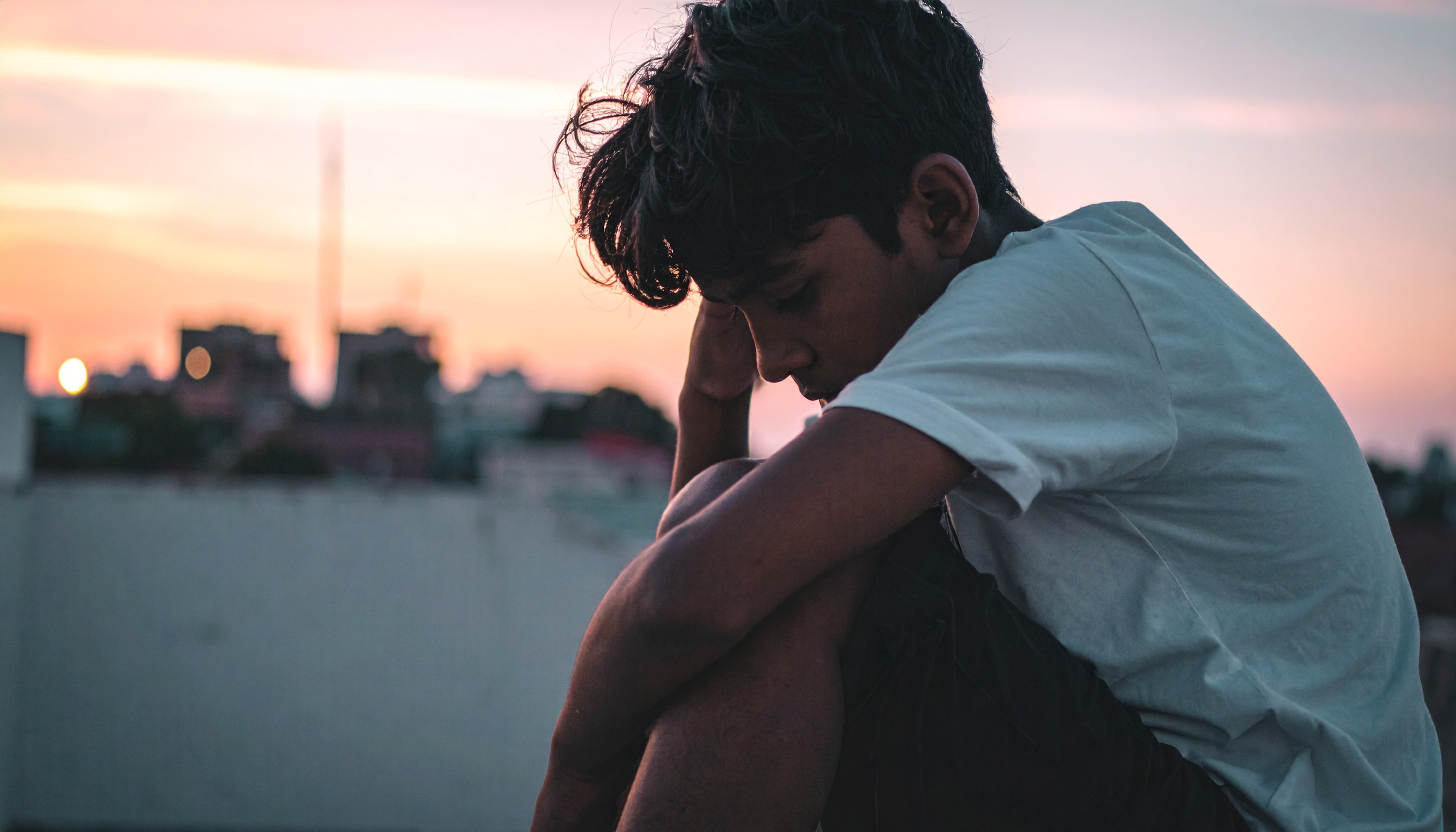 A young person sits thoughtfully against a sunset backdrop